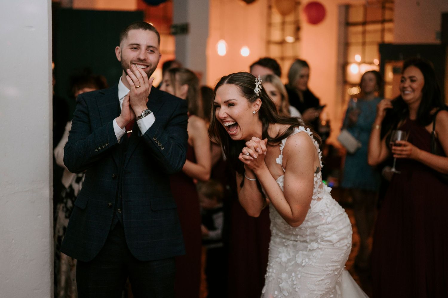 Bride and groom react with delight and laughter during a fun moment at their wedding reception.