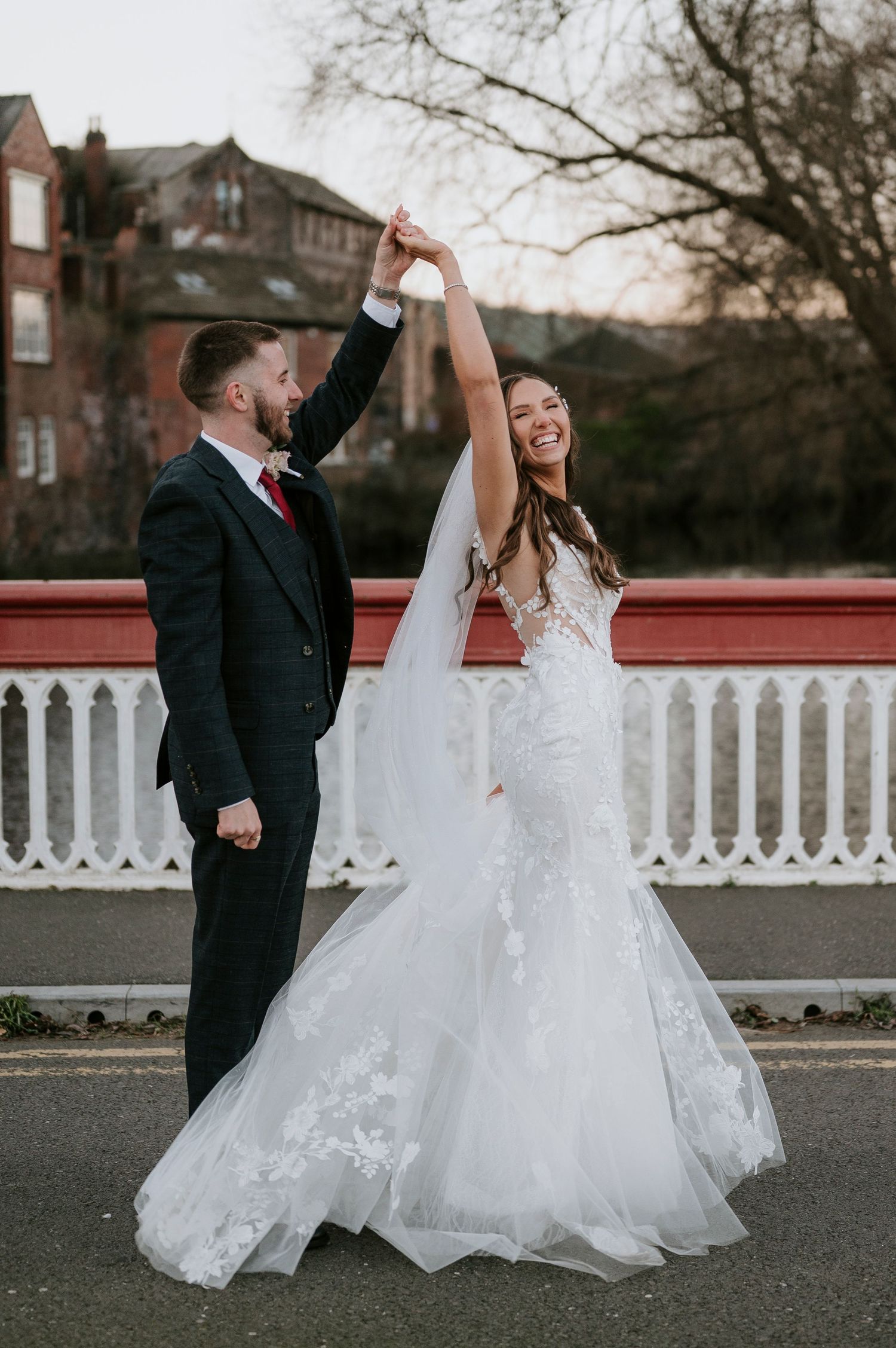 A joyful newlywed couple celebrates on a bridge with a white balustrade during their wedding photoshoot.