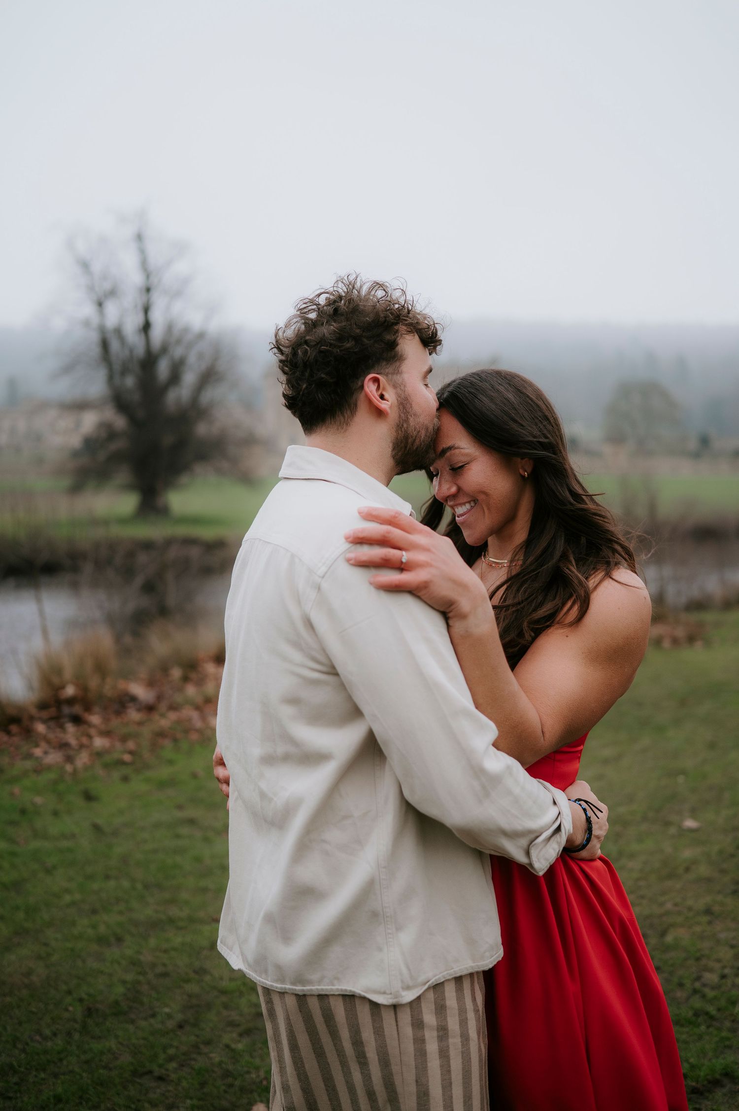 A couple in red and white attire share intimate moments while dancing together in a misty outdoor field.