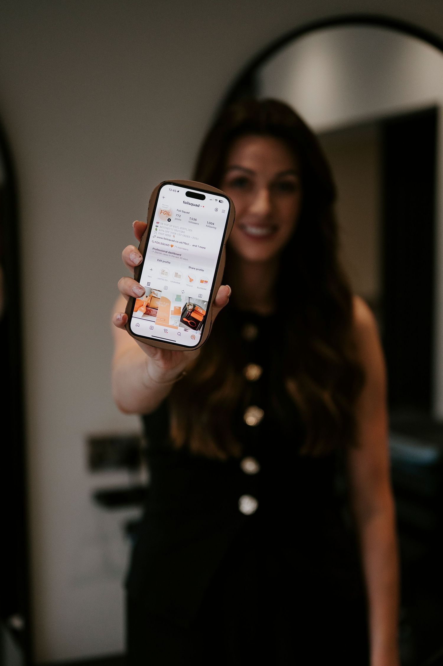 Person in black top holding up a phone displaying a social media interface in a dimly lit setting.