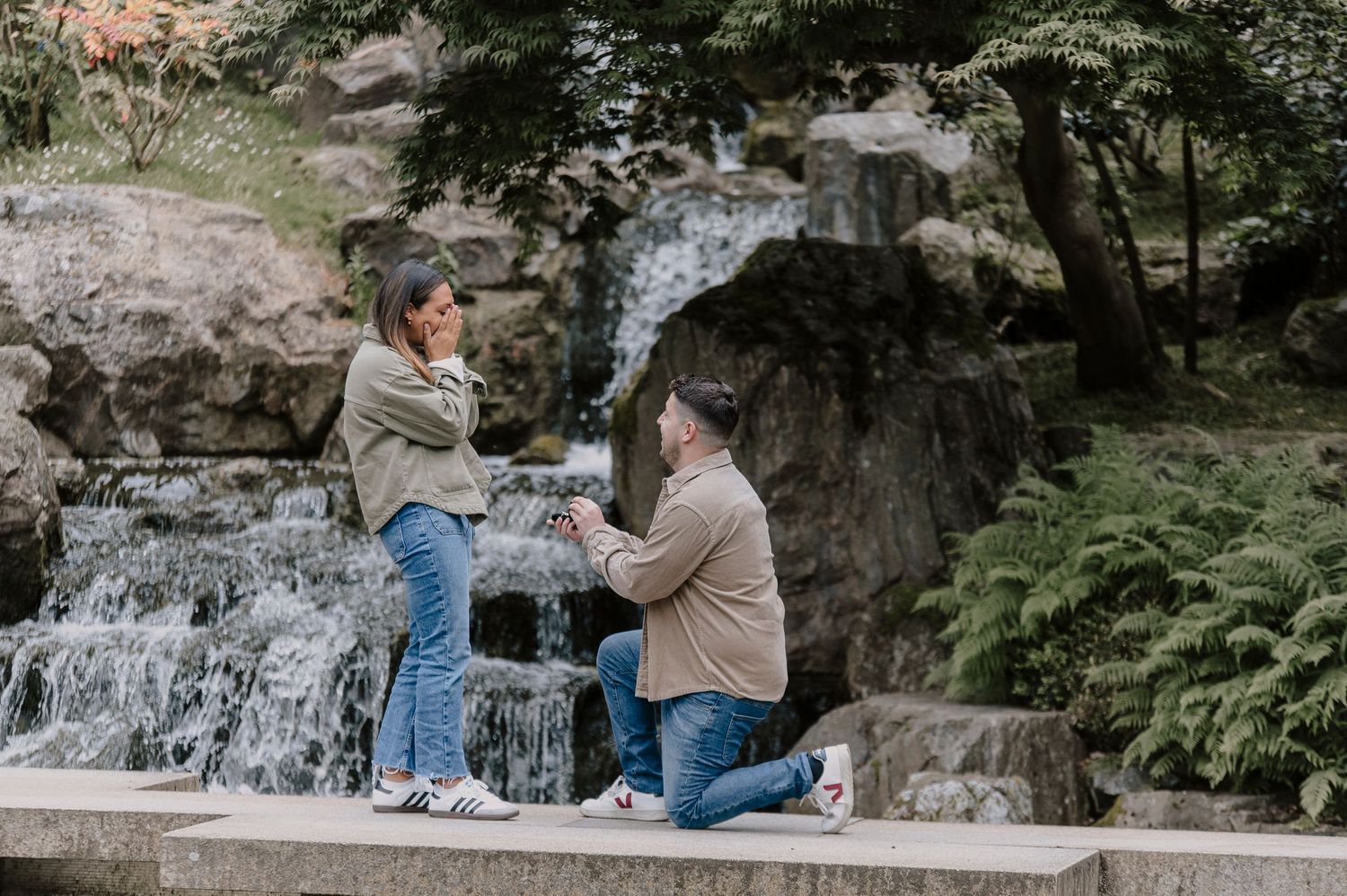 A romantic proposal moment captured by a waterfall in a lush garden setting.