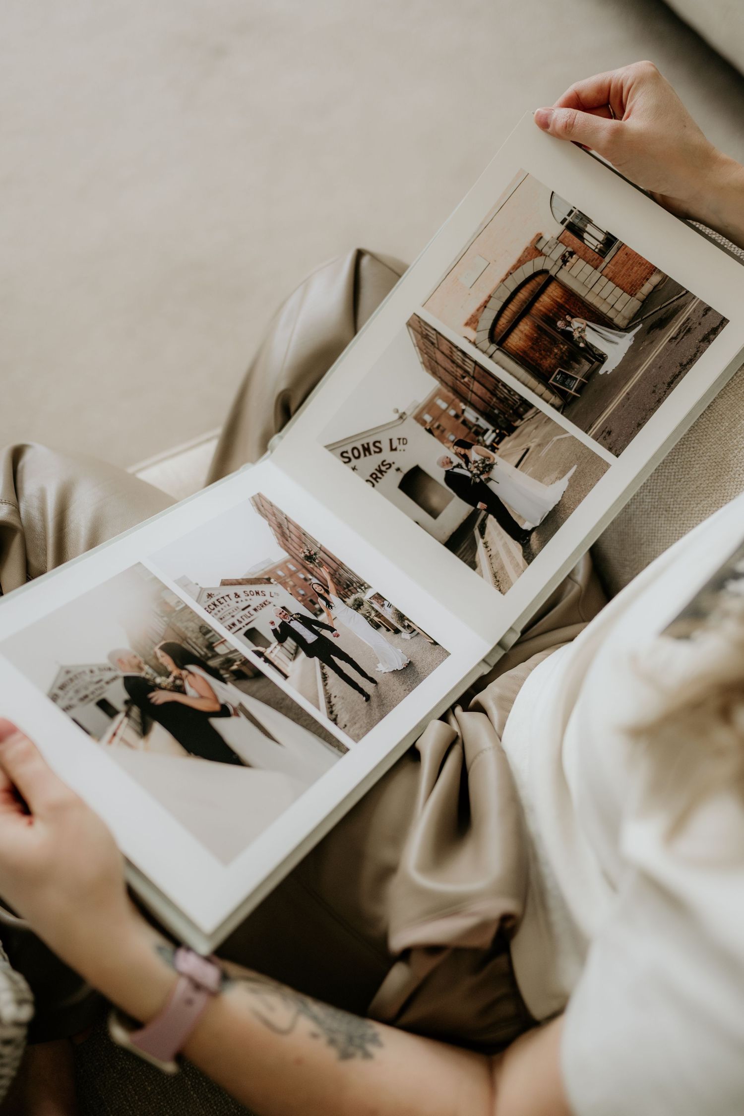 Someone in a white sweater flips through a photo album containing black and white photographs on cream colored pages.