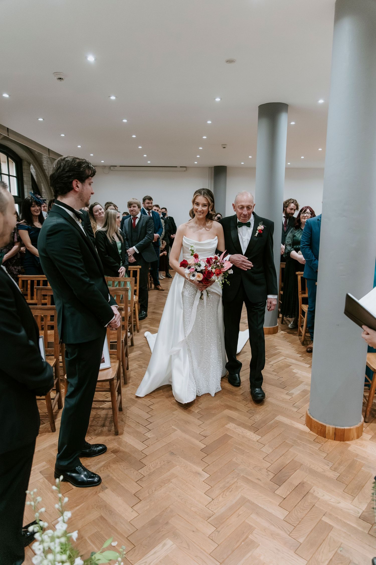 Elegant wedding ceremony in a contemporary space with guests gathered around pillars and parquet flooring.