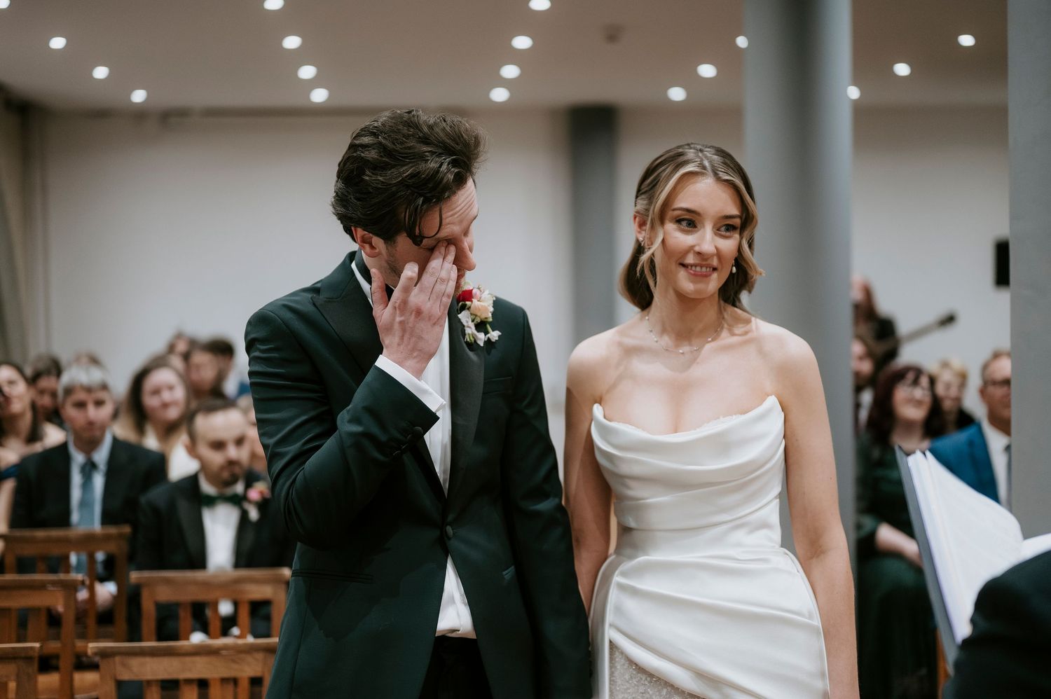 Wedding couple stands at altar during indoor ceremony with guests seated in church pews.