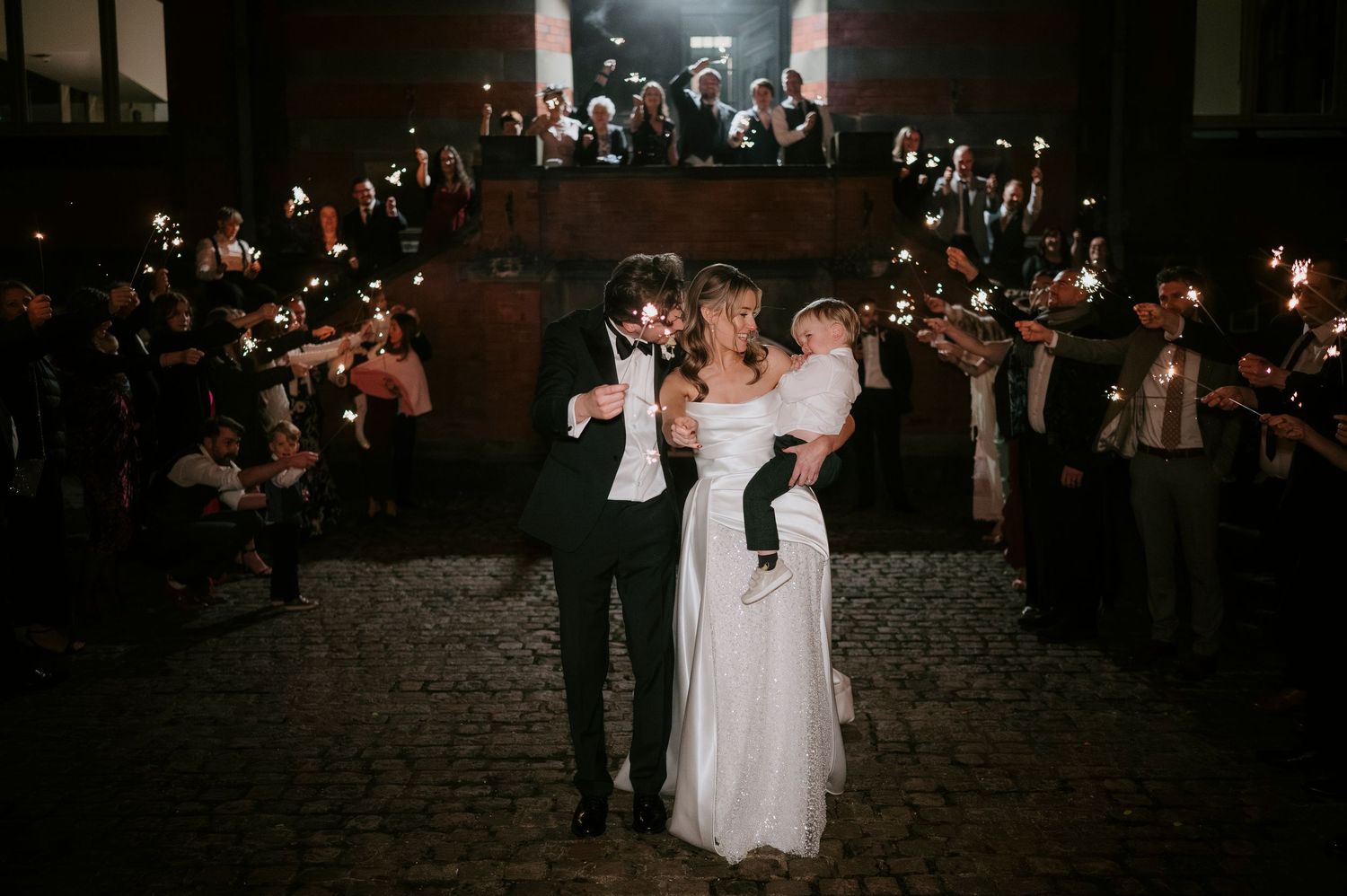 A dark reception hall filled with wedding guests dancing and celebrating at night.