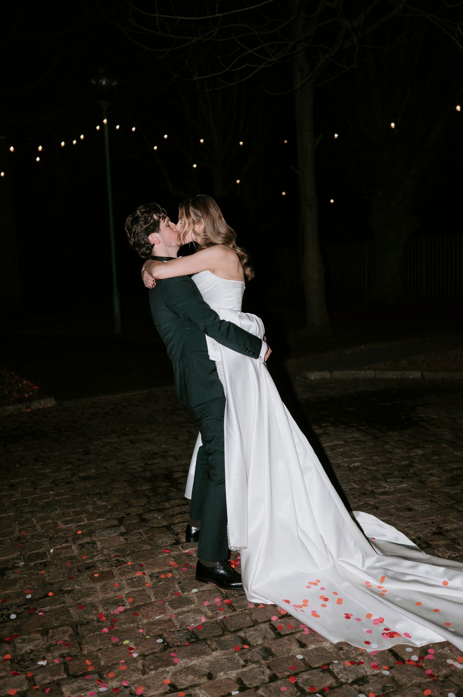 A romantic dance dip on cobblestones with rose petals scattered around during a nighttime celebration.