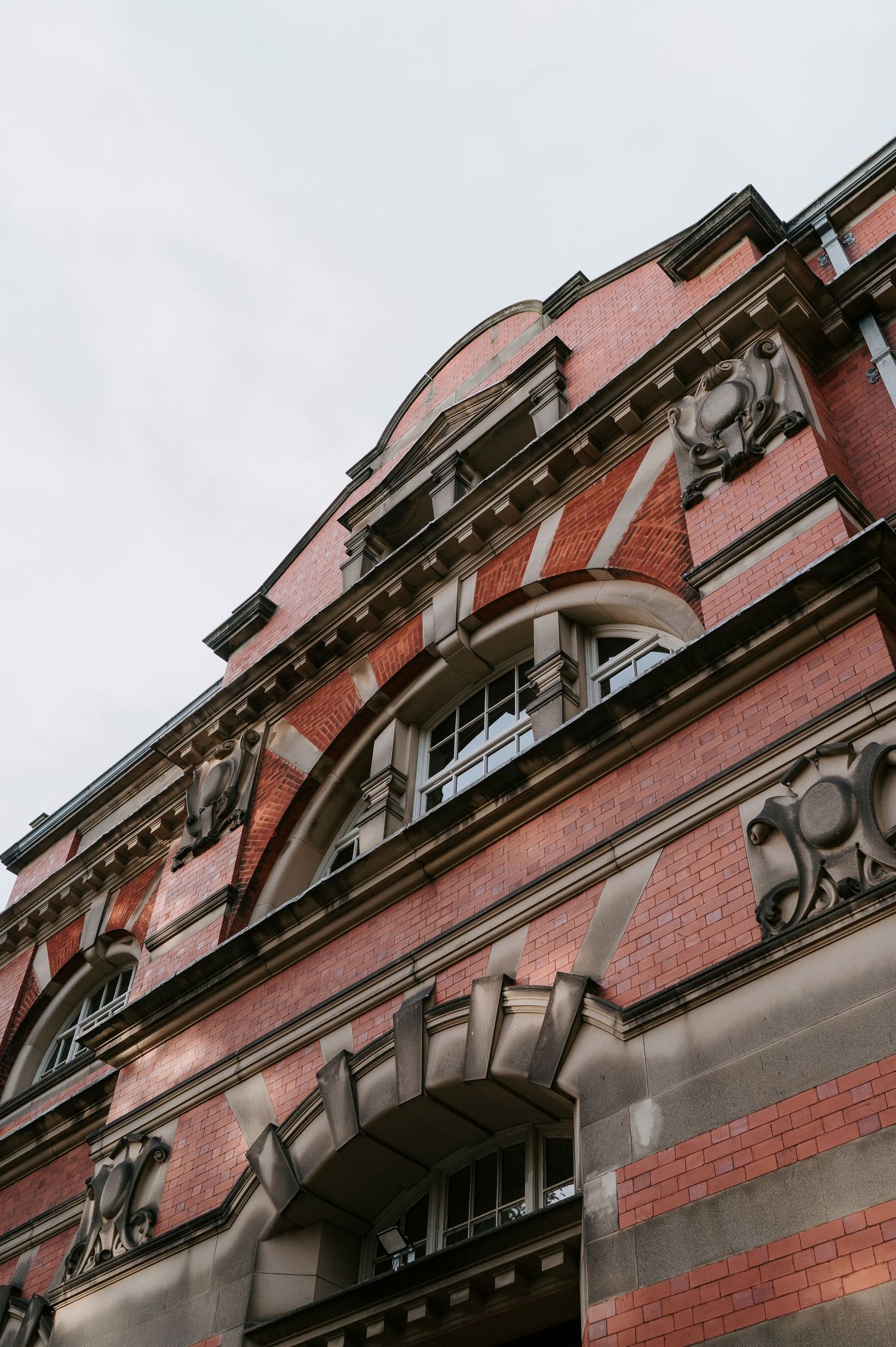 Historic red brick building facade with ornate architectural details and arched windows against cloudy sky.