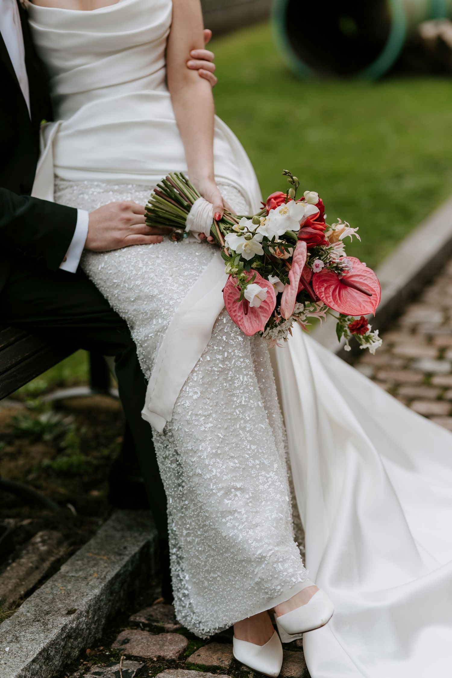 Close-up details of white wedding dress and pink floral bouquet against rustic backdrop.