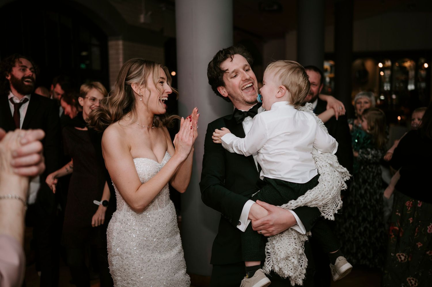 A joyful moment at a wedding reception with a couple and small child celebrating together.