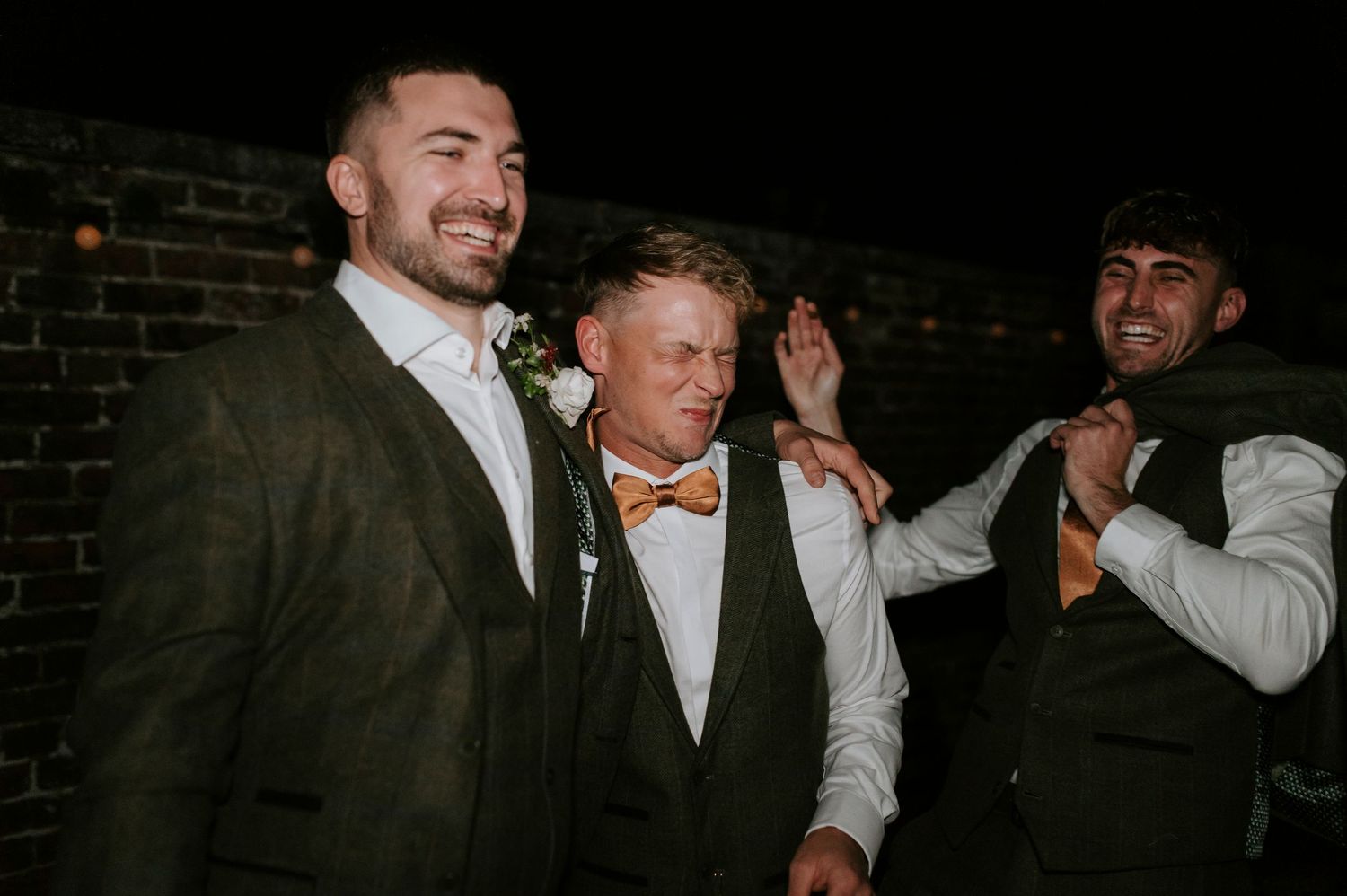 A group of people laughing and celebrating at a dimly lit party venue with brick walls in the background.