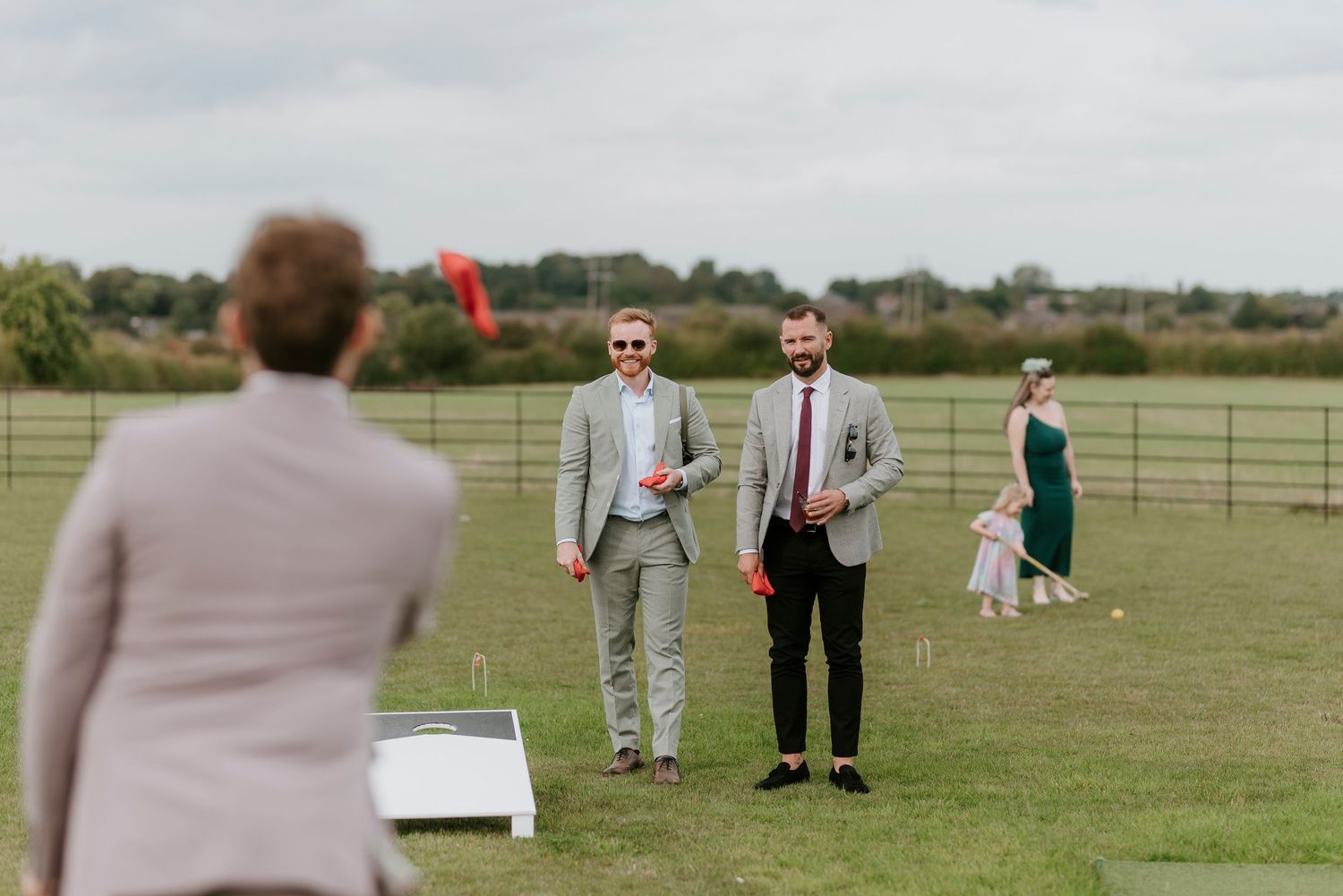 Wedding guests mingle and socialize on a grassy field during an outdoor celebration on a sunny day.