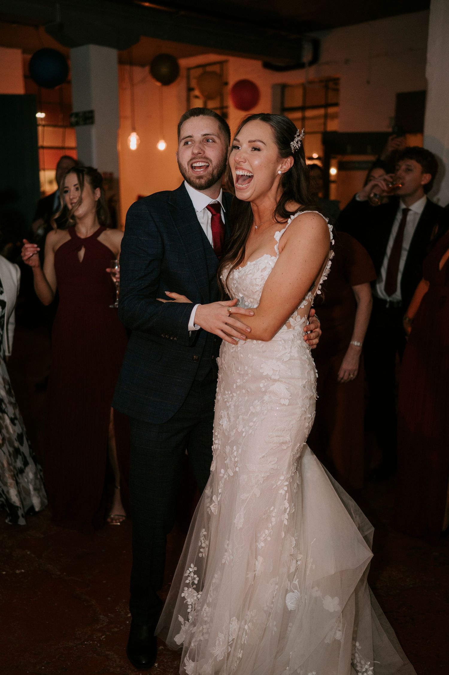 Bride and groom laughing joyfully on the wedding dance floor, bride wearing a lace mermaid gown.