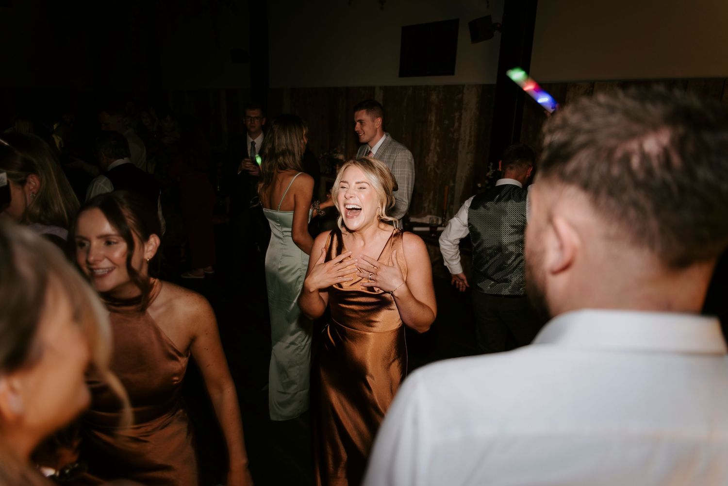 People dancing and laughing at a wedding reception party with festive lighting in a dark venue.