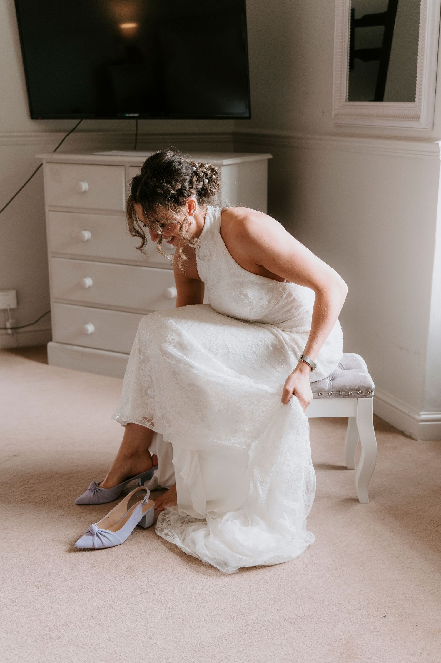 A bride in a white wedding dress sits on the floor while putting on her bridal shoes.