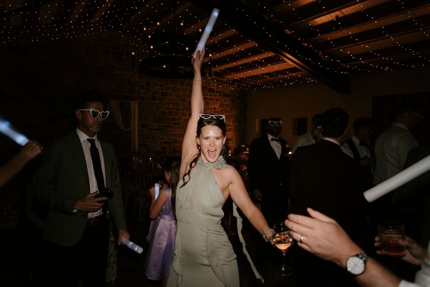 Couple celebrating at a lively wedding reception with guests dancing in a dimly lit venue.