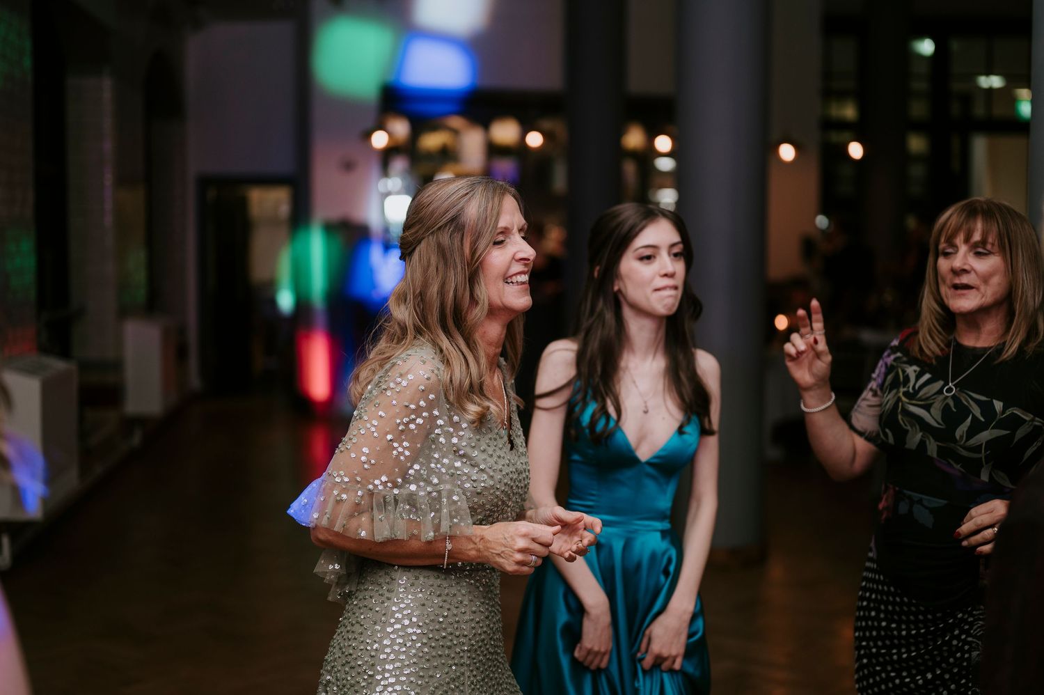 Wedding guests in elegant dresses enjoying themselves at an evening celebration with ambient lighting.