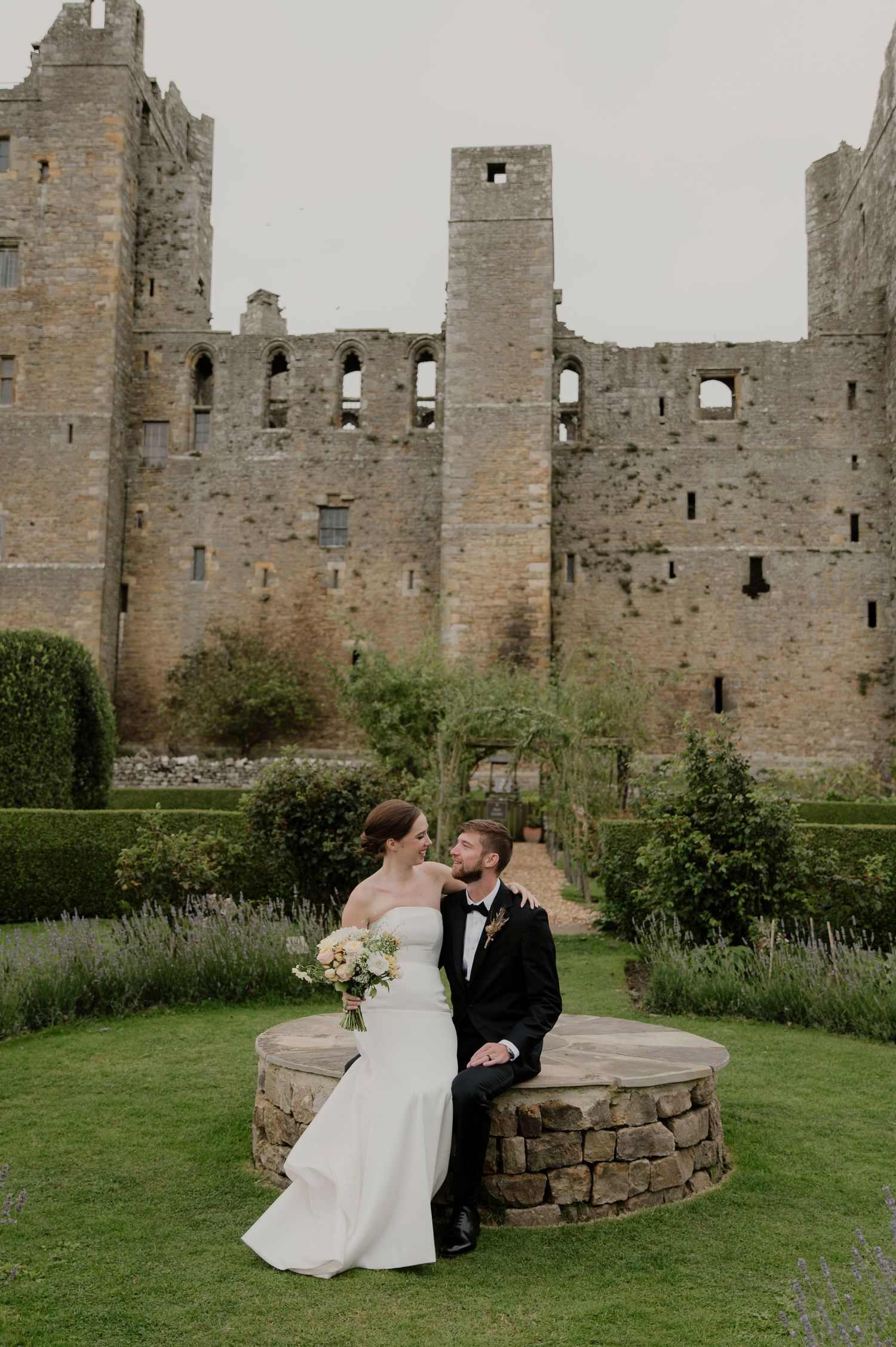 Romantic wedding portraits taken in front of ancient castle ruins with stone walls and green lawn.