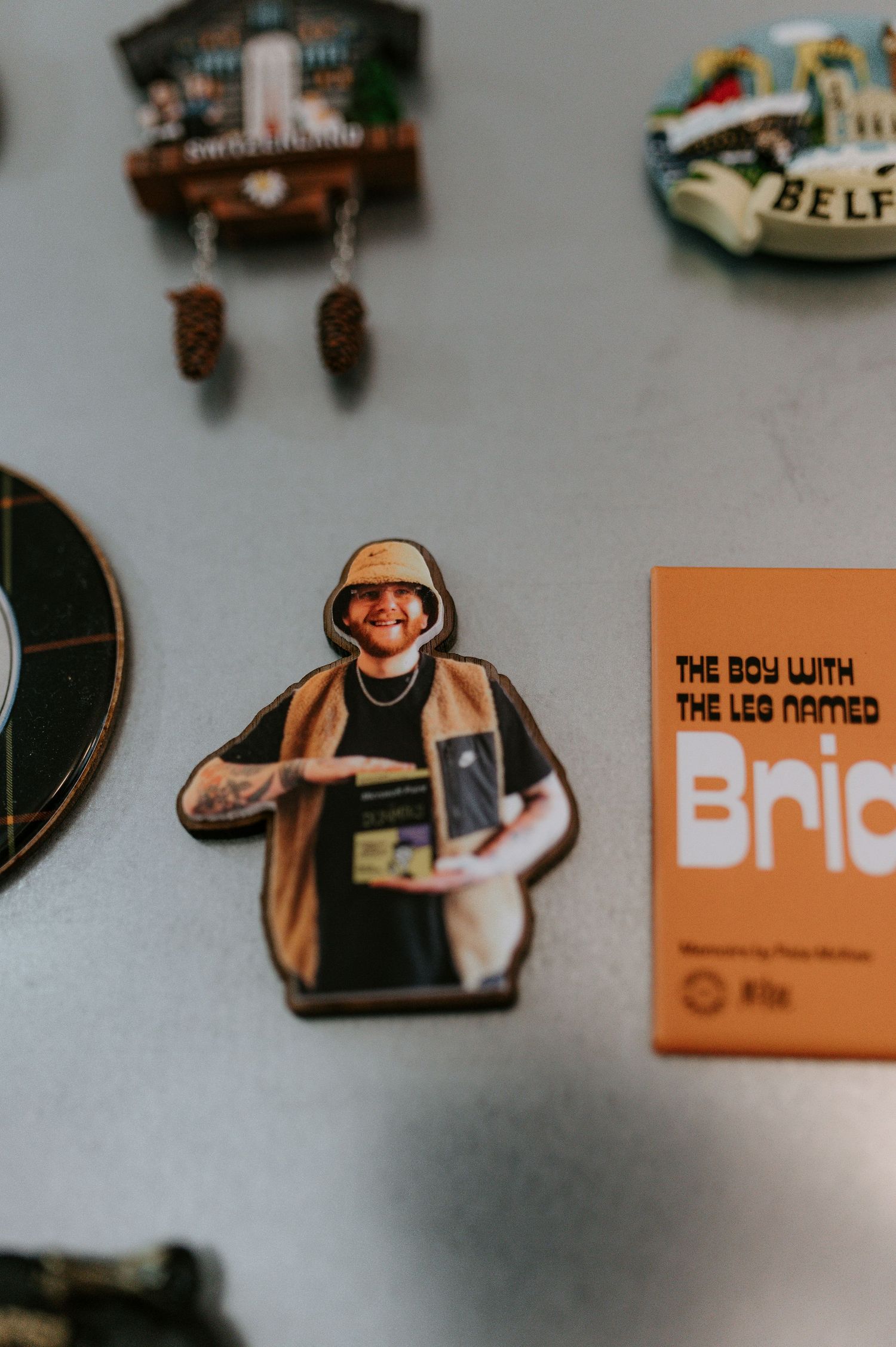 A decorative magnet or pin on display shows a figure in a beige coat next to other souvenir items on a wall.