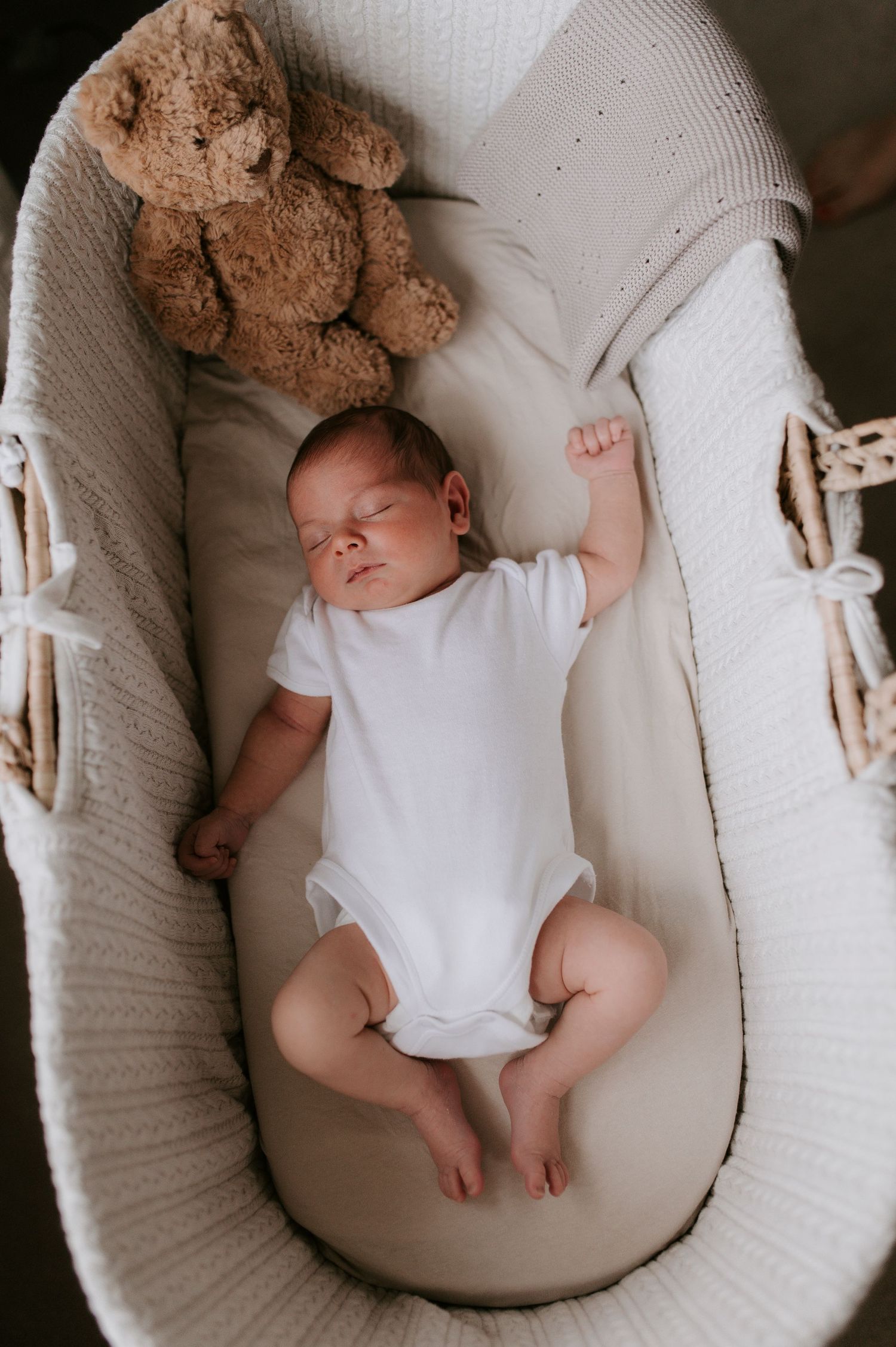 A sleeping baby in white onesie rests peacefully in a cream-colored bassinet viewed from different angles.