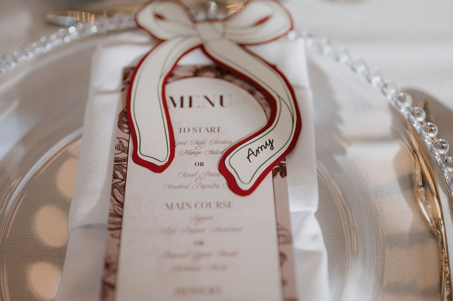 Wedding menu cards with red ribbon bows displayed on elegant place settings.