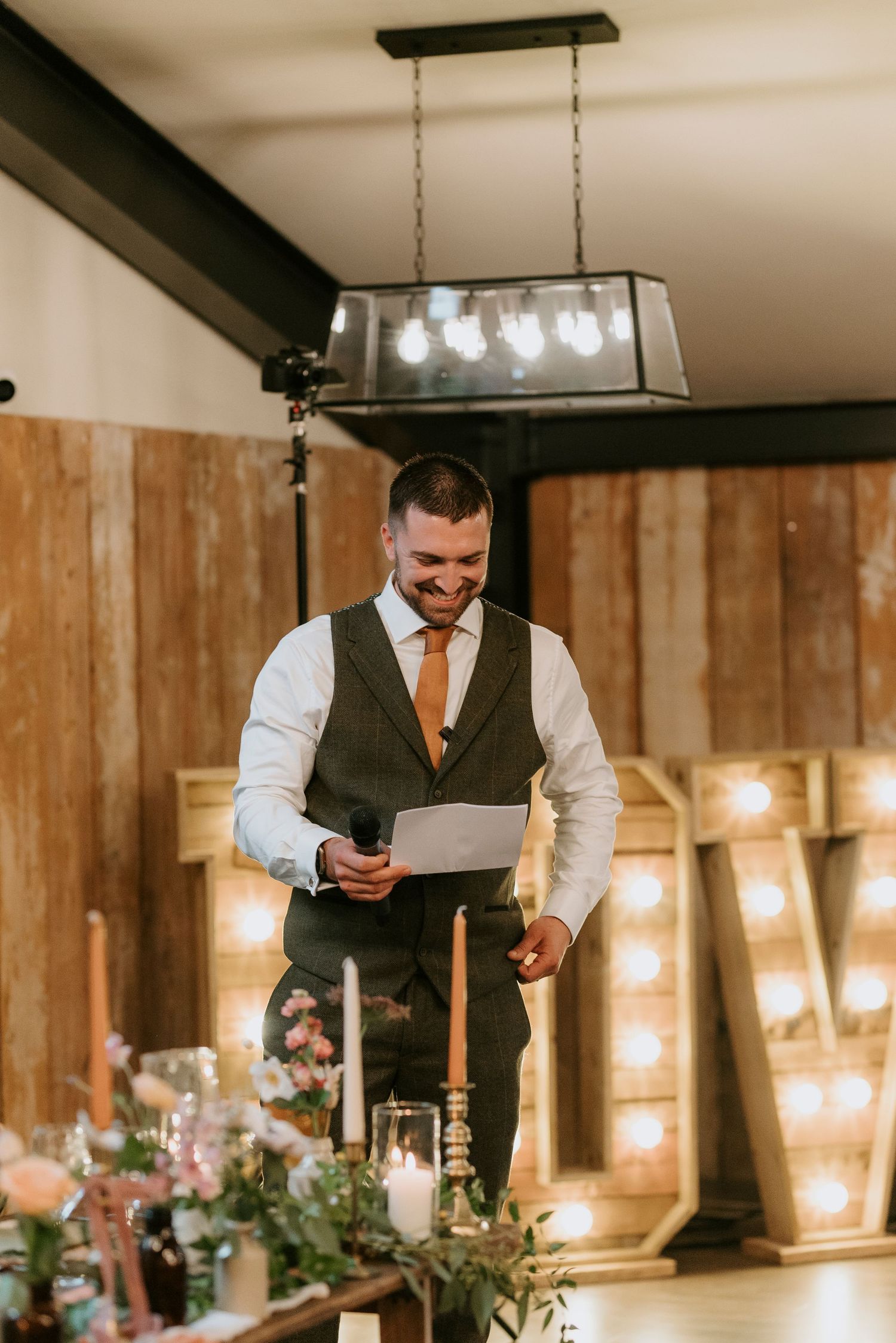 Wedding reception venue decorated with rustic wood paneling and warm pendant lighting creates an intimate atmosphere.