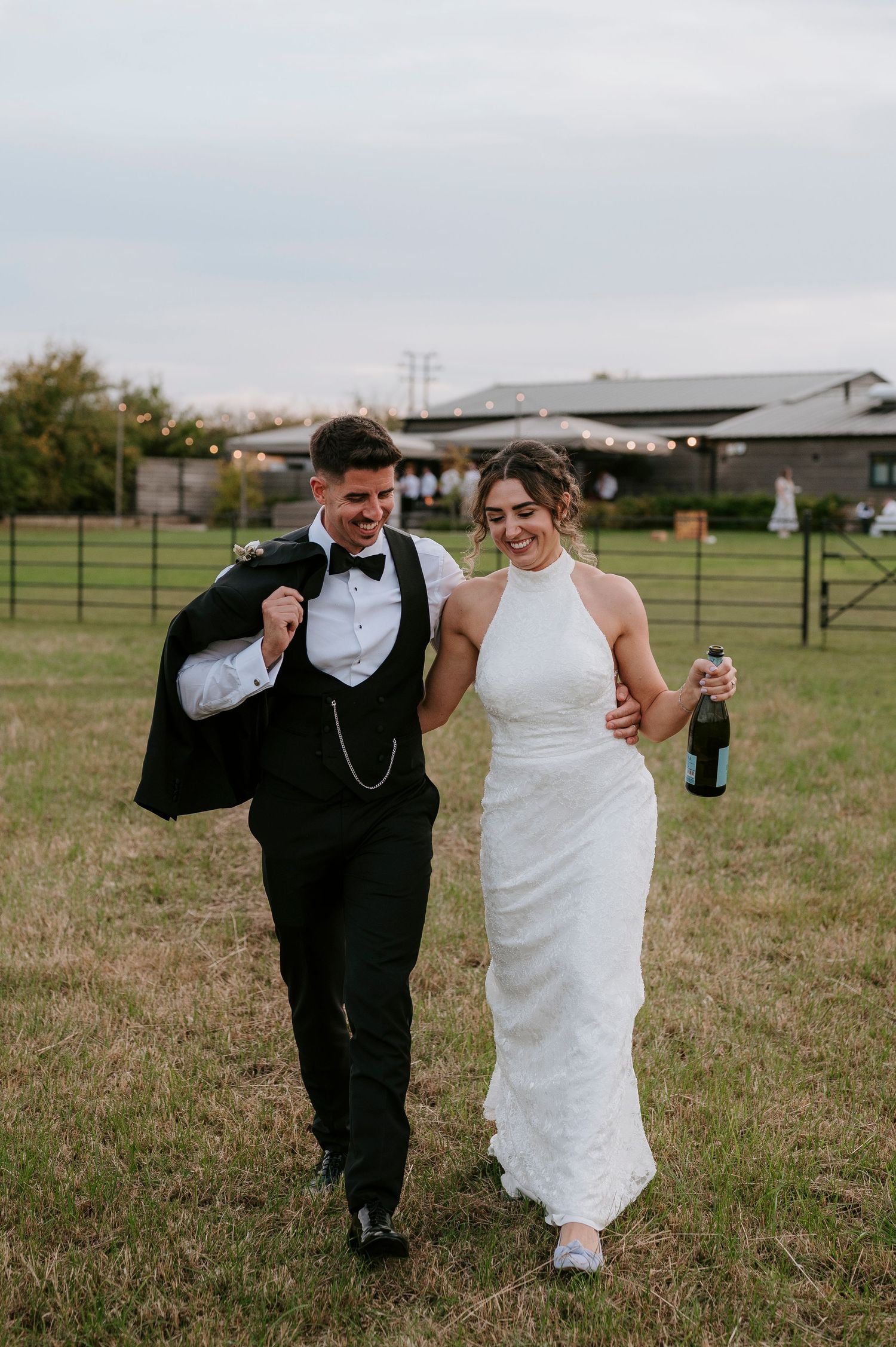 Two people in wedding attire share a joyful moment while walking together in a grassy field.