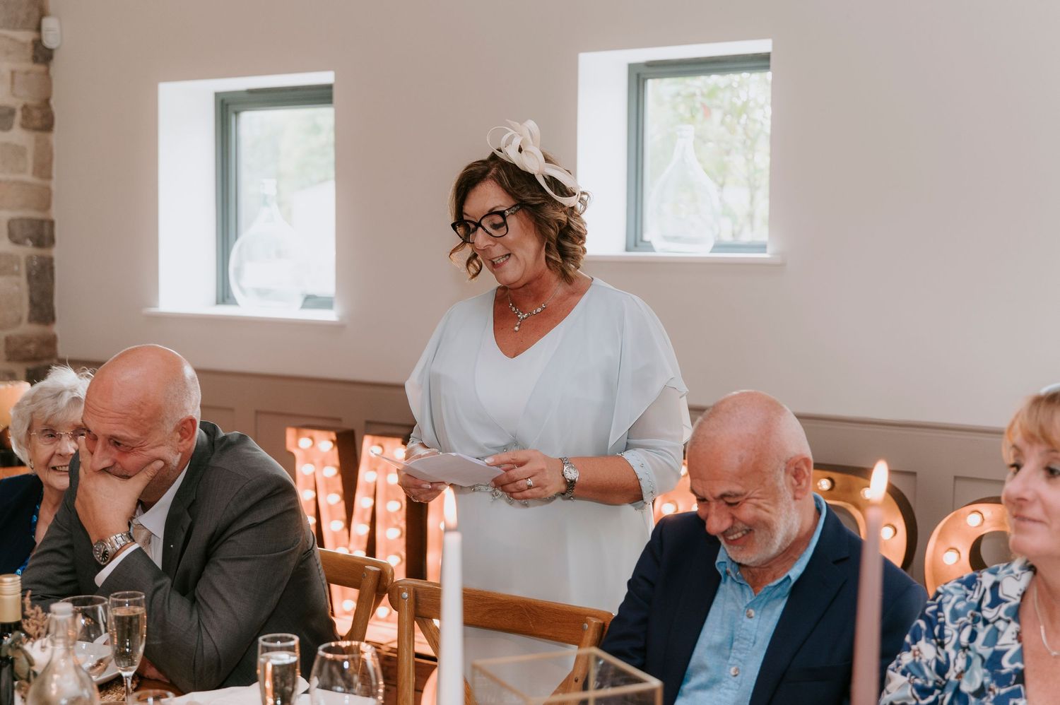 People enjoying a meal and conversation at a long communal dining table in a bright, airy restaurant setting.
