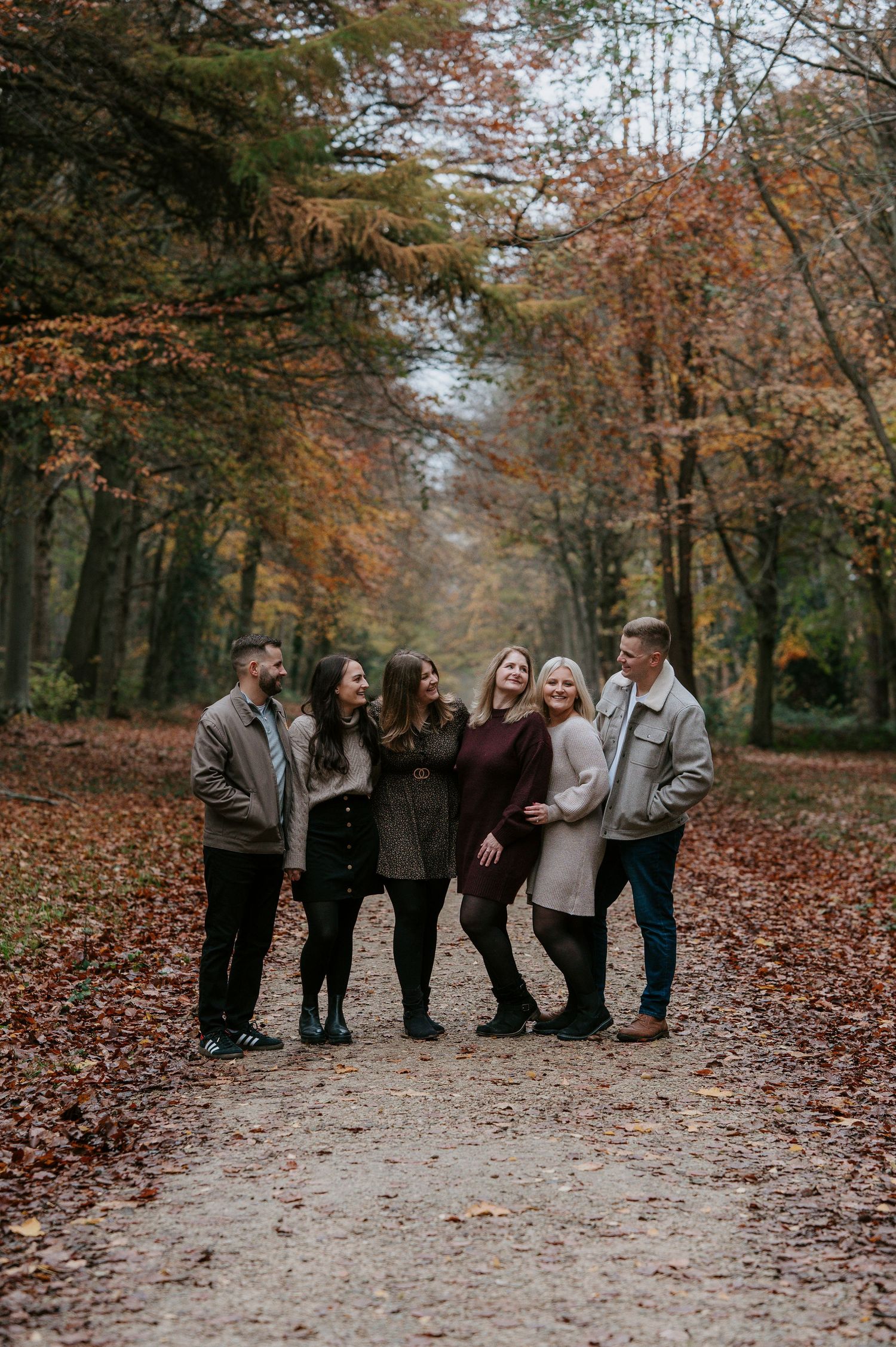 Friends gathered on a wooded trail surrounded by fallen autumn leaves and trees with changing colors.