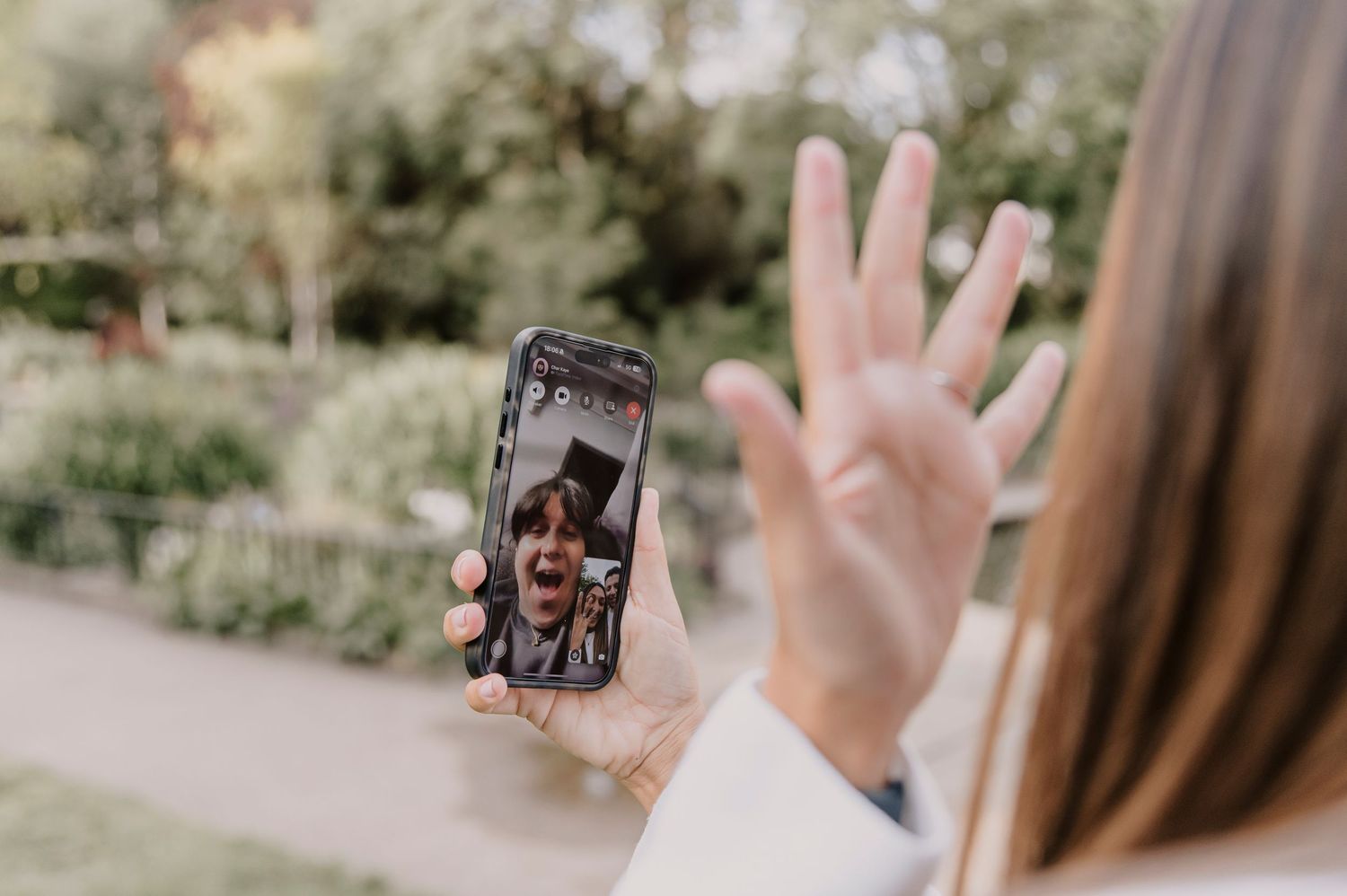 Person holding up smartphone for video chat while walking in sunny outdoor garden setting.