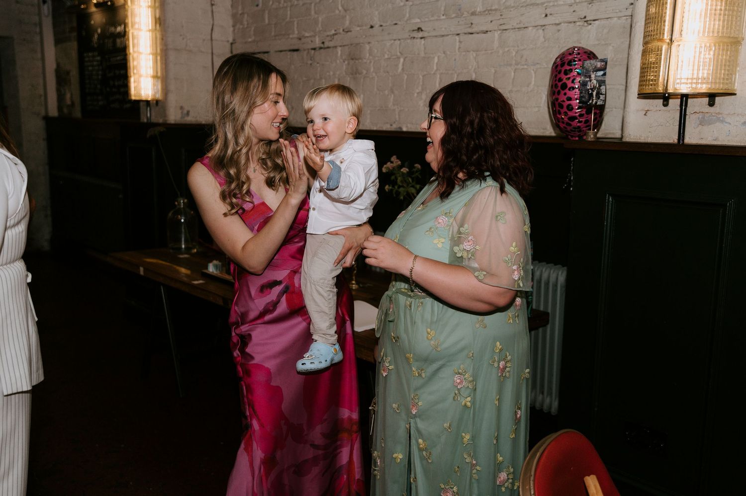 Two people in formal attire share a moment with a small child at an indoor event.