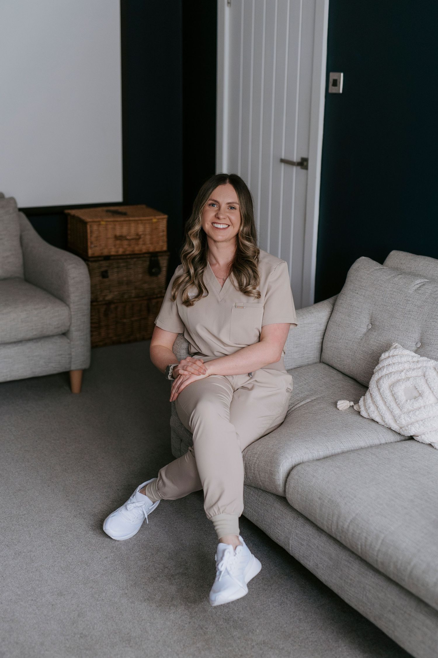 A person in neutral-colored loungewear sits casually on a gray couch in a minimalist room setting.