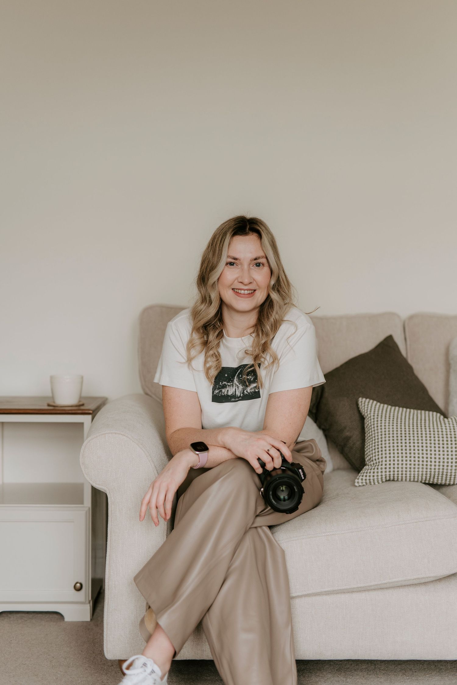 A person in casual attire sits comfortably on a white couch with throw pillows in a minimalist room setting.