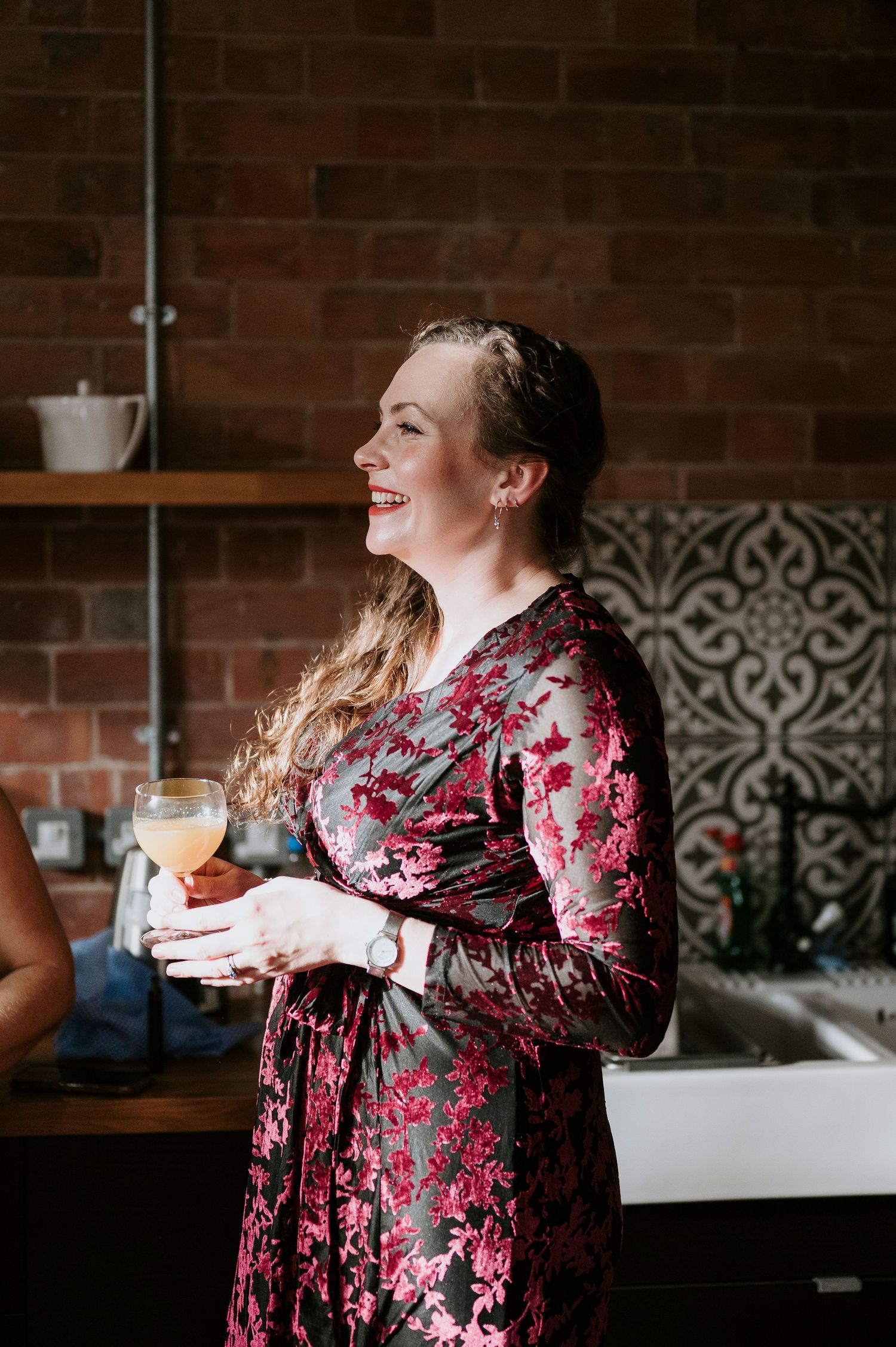 Candid moments captured of someone wearing a floral burgundy dress in an industrial-style space with brick walls.