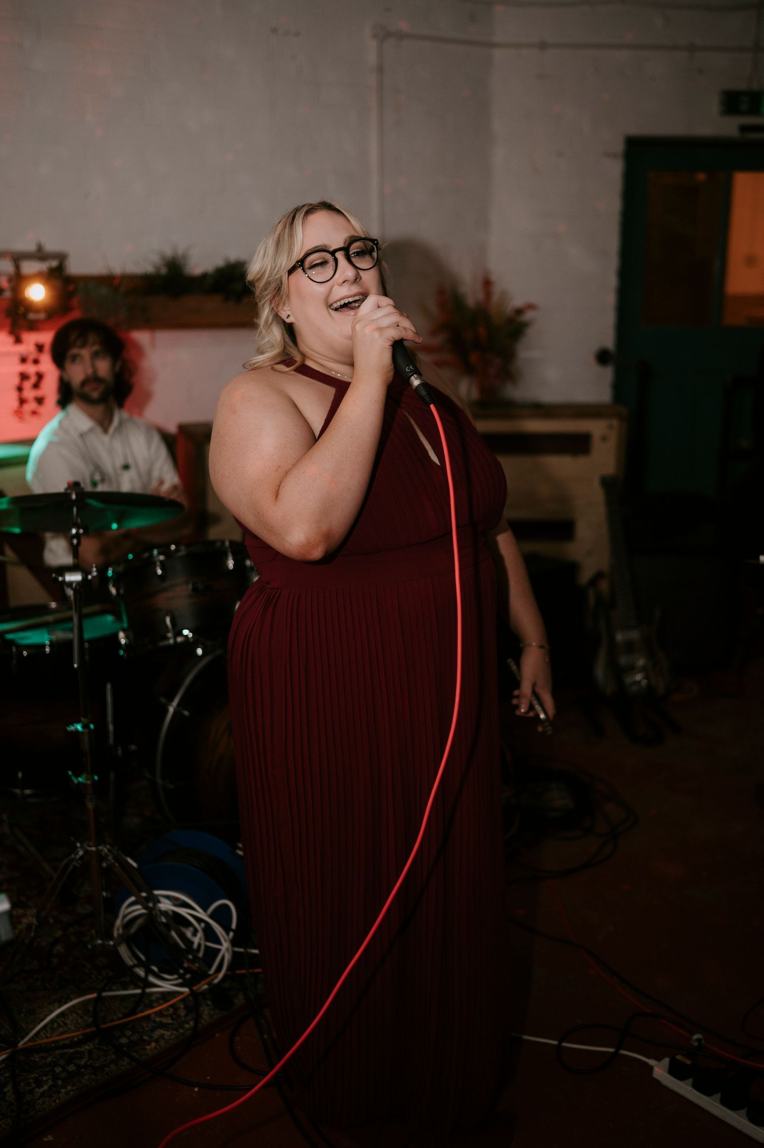 A female singer in a burgundy gown performs with a microphone at a wedding reception.
