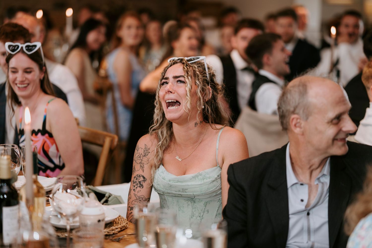 Wedding reception guests laugh and smile while enjoying dinner and drinks at a lively celebration.