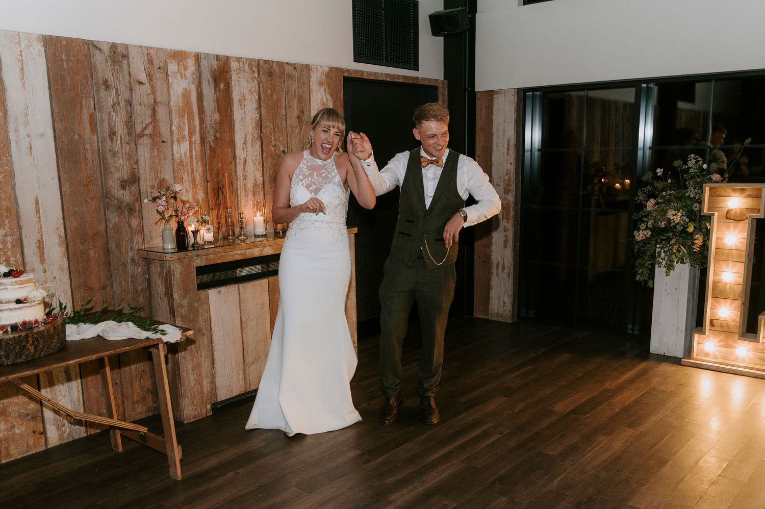 A couple shares a joyful moment dancing together in a rustic venue with wooden walls and illuminated decor.