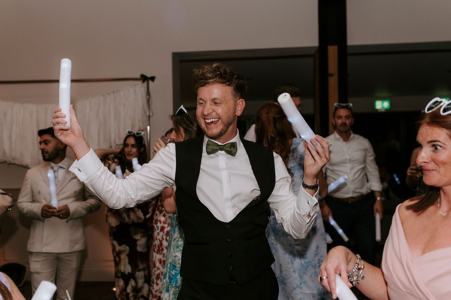 Wedding guests dance and celebrate with raised arms on a lively dance floor at an indoor reception.