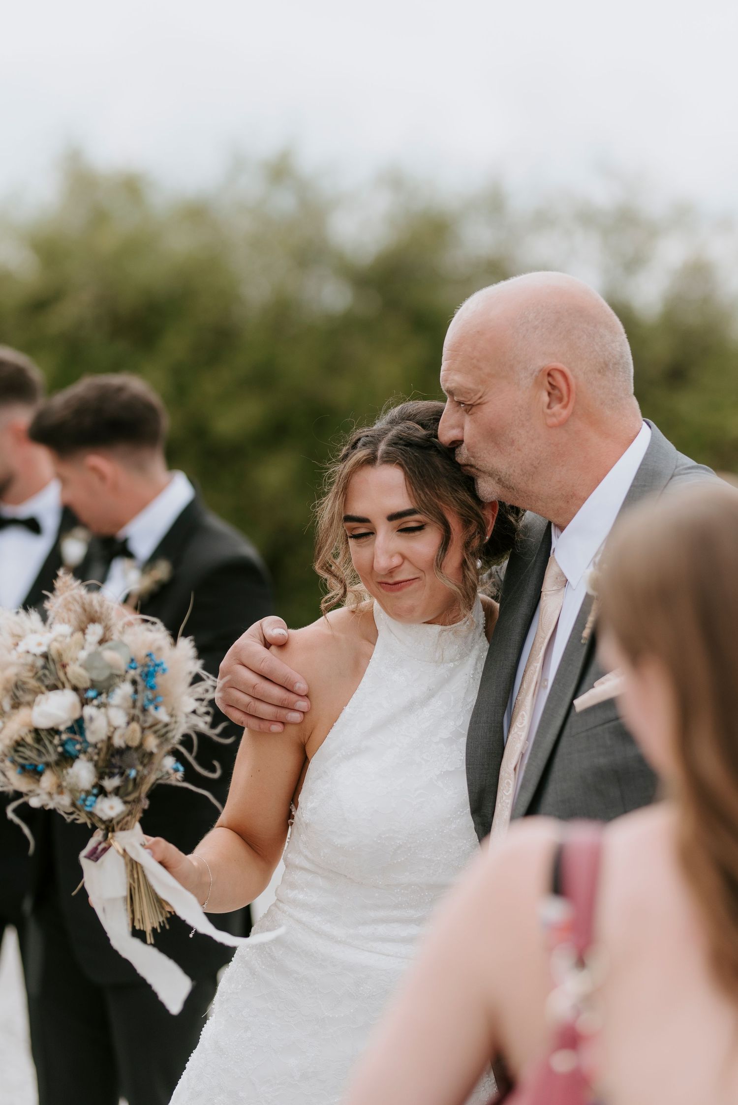 A happy couple shares an emotional moment during their outdoor wedding ceremony with guests looking on.