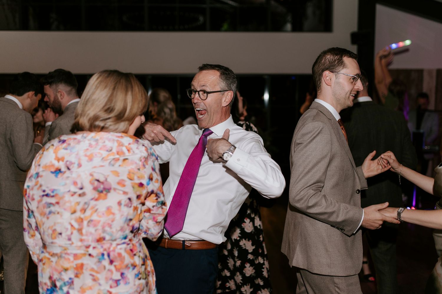 Couples dance together in a dimly lit room during what appears to be a wedding reception or social gathering.