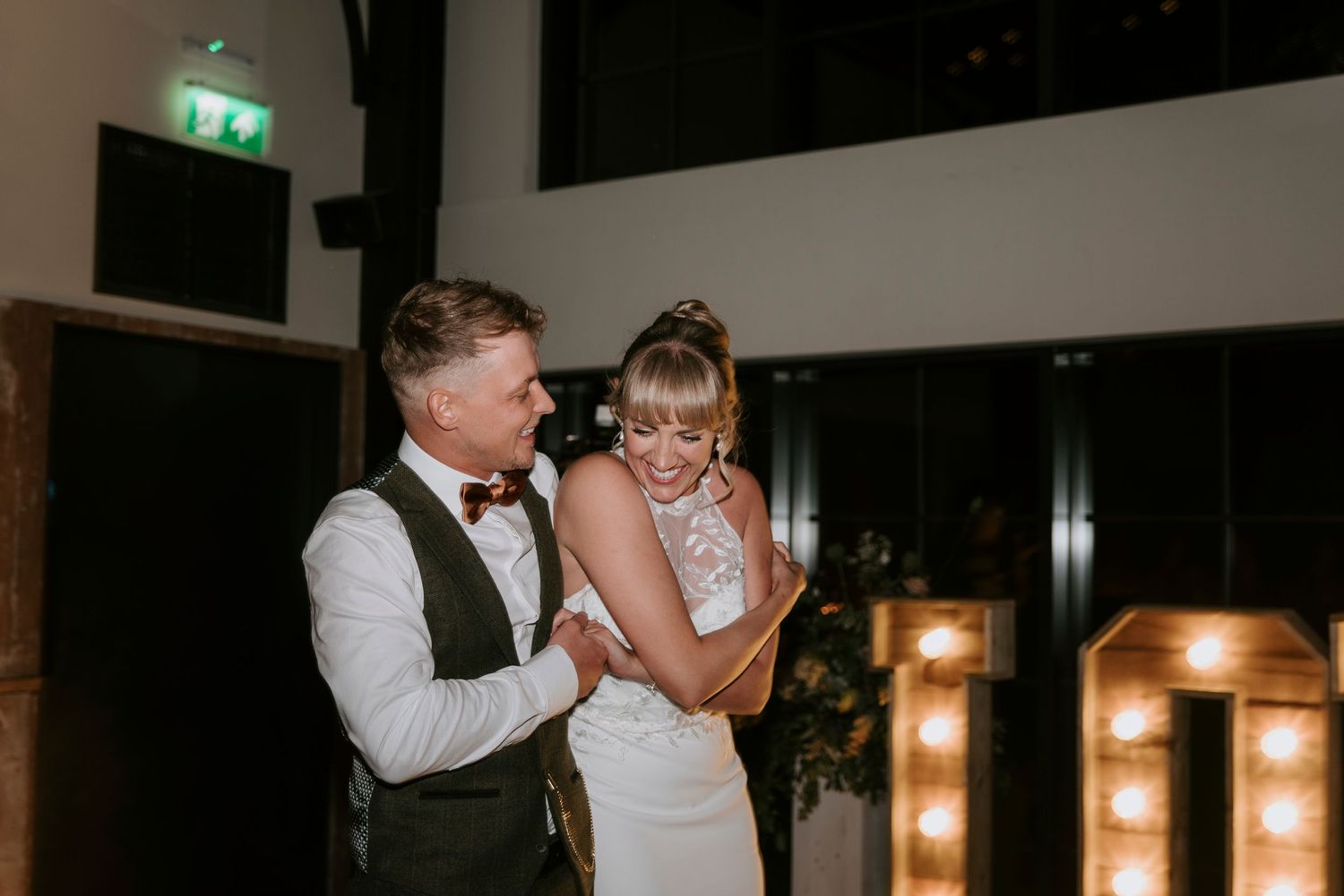 A couple shares an intimate dance moment during their wedding reception in a dimly lit venue with warm glowing lights.