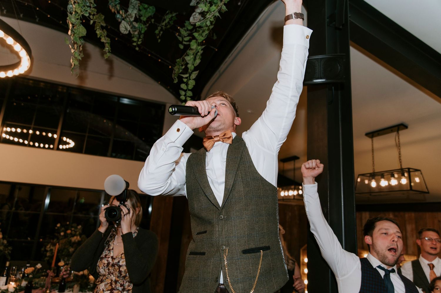 A group of people raise their glasses in celebration during a wedding reception at an indoor venue.