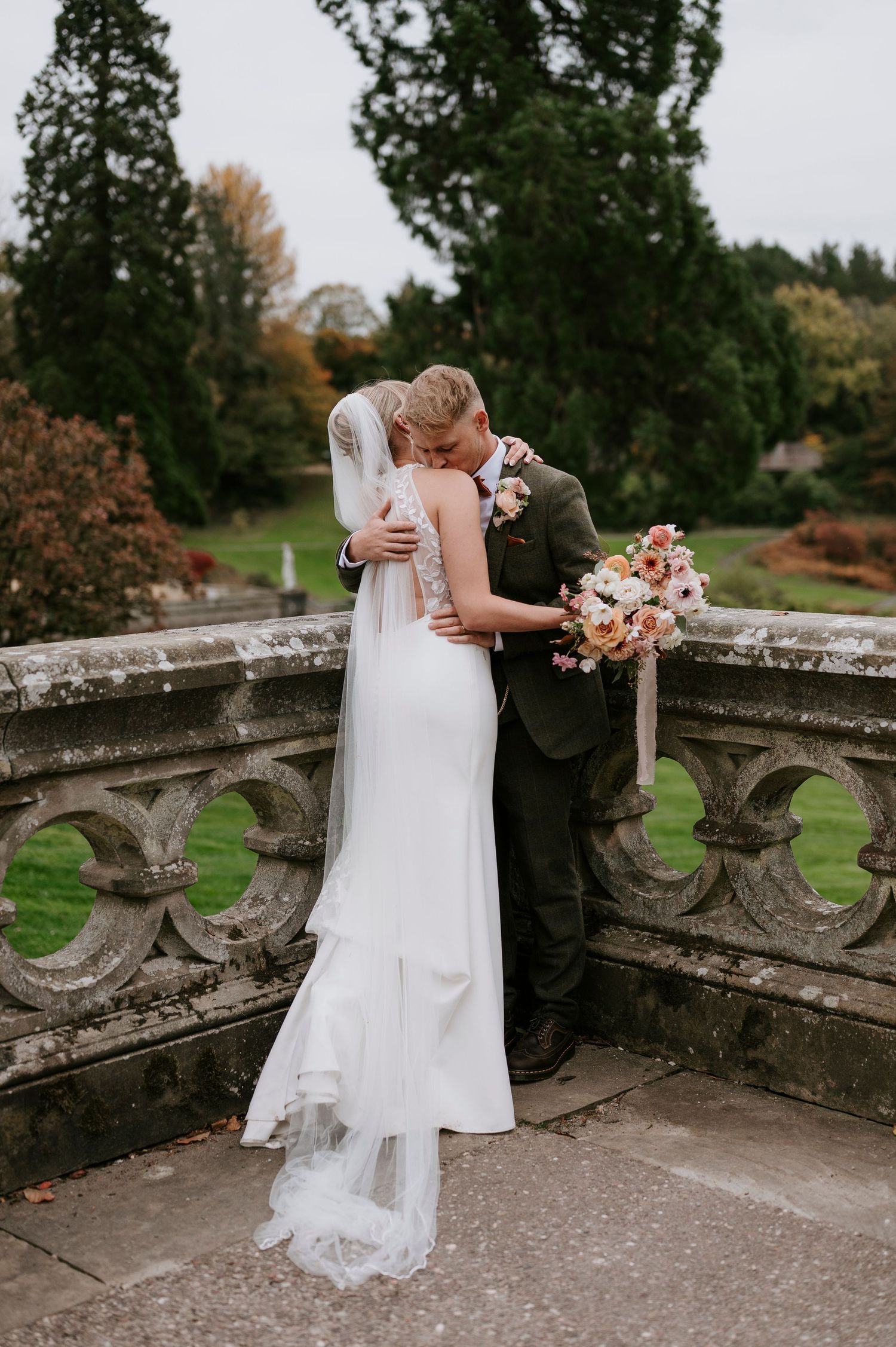 Romantic couple shares intimate moment on stone balcony during autumn wedding at historic venue.