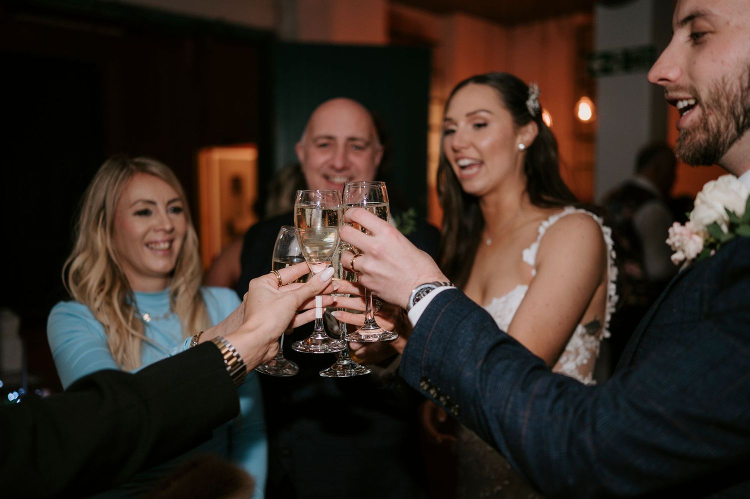 Wedding guests toasting with champagne glasses, bride in white dress celebrating with friends at reception.