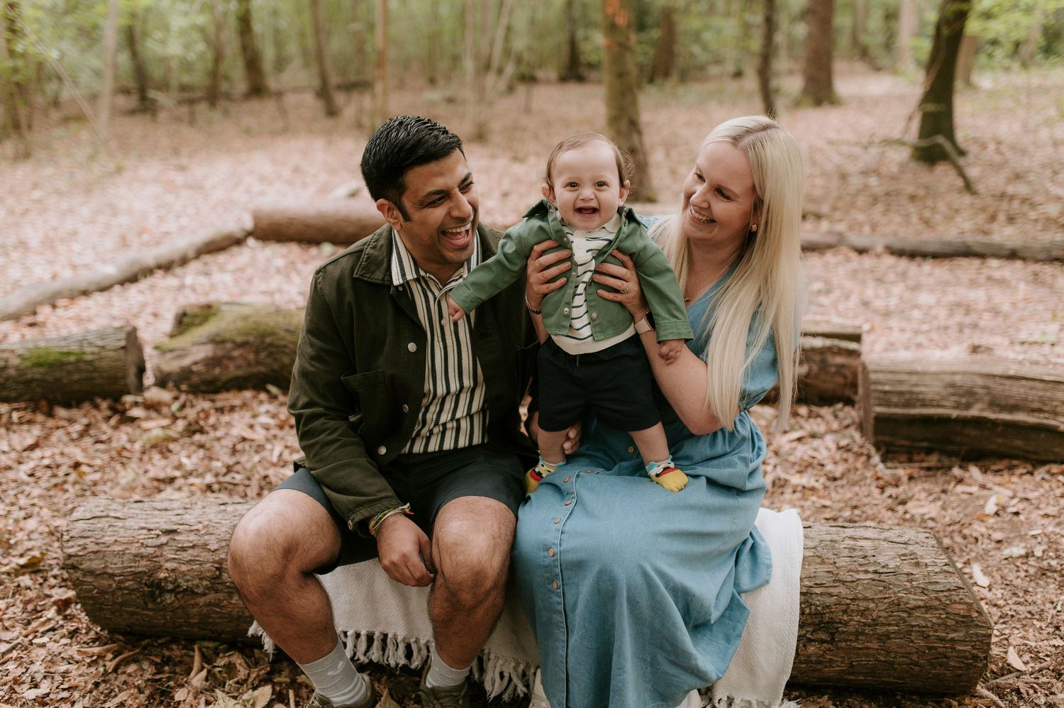 A family shares joyful moments together while sitting on fallen logs in a peaceful forest setting.