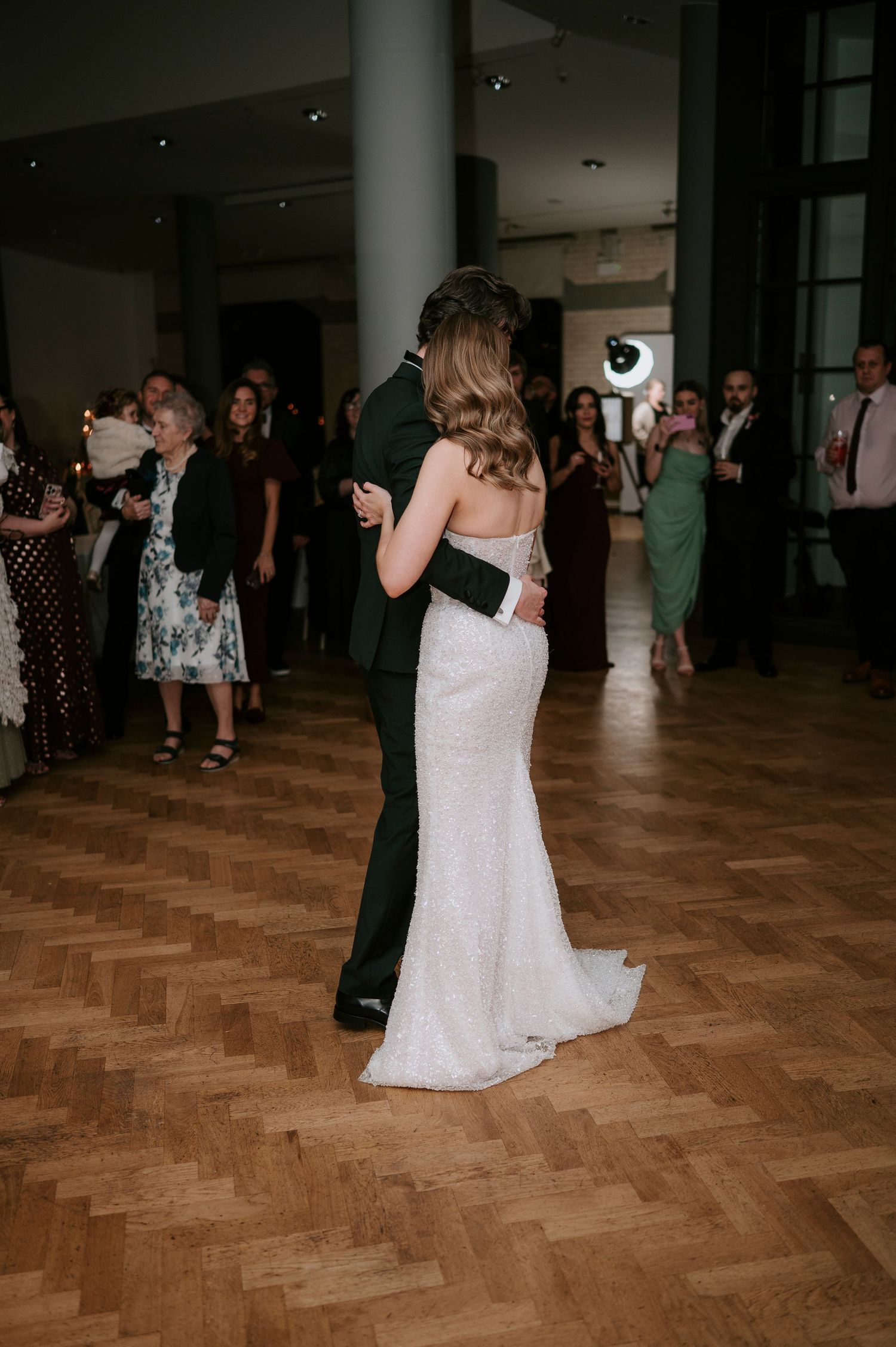 A couple shares their first dance at a wedding reception on a parquet dance floor.