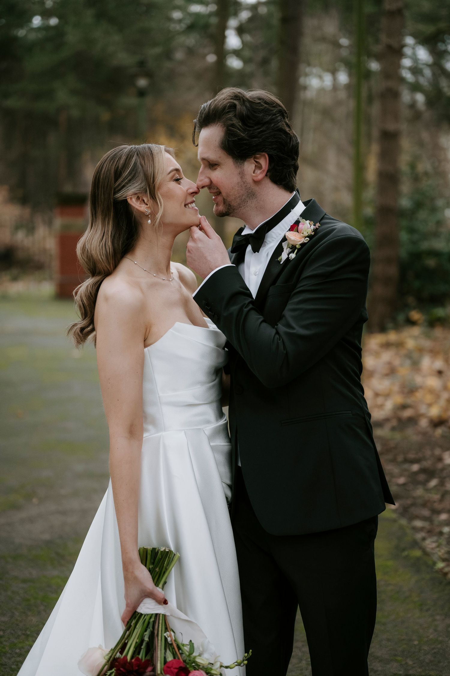 Romantic wedding couple shares intimate moments in a wooded outdoor setting with fallen leaves.