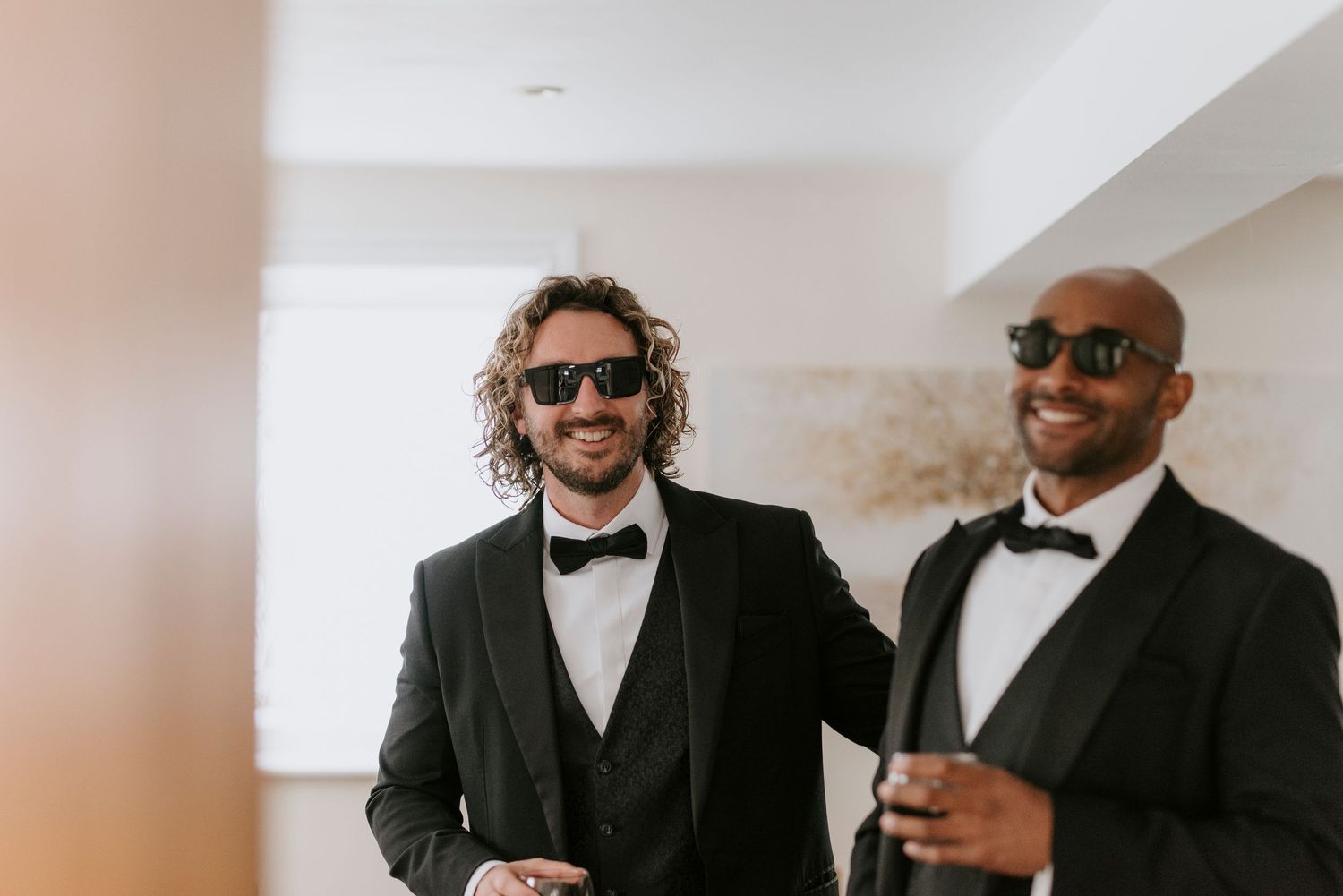 Two well-dressed men in black tuxedos and bow ties share a joyful moment at a formal event.