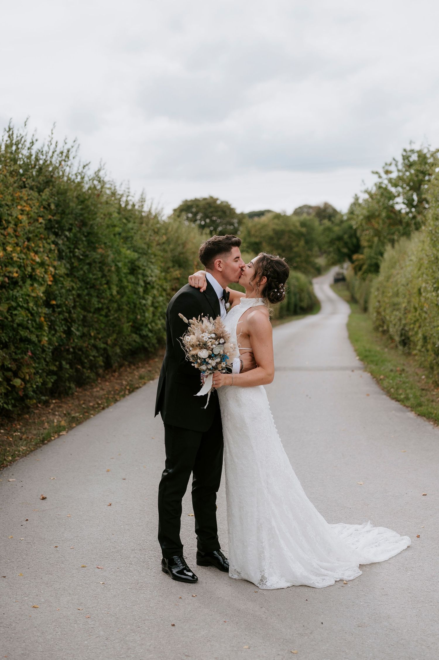 A romantic couple shares an intimate moment on a tree-lined country path during their wedding photo session.