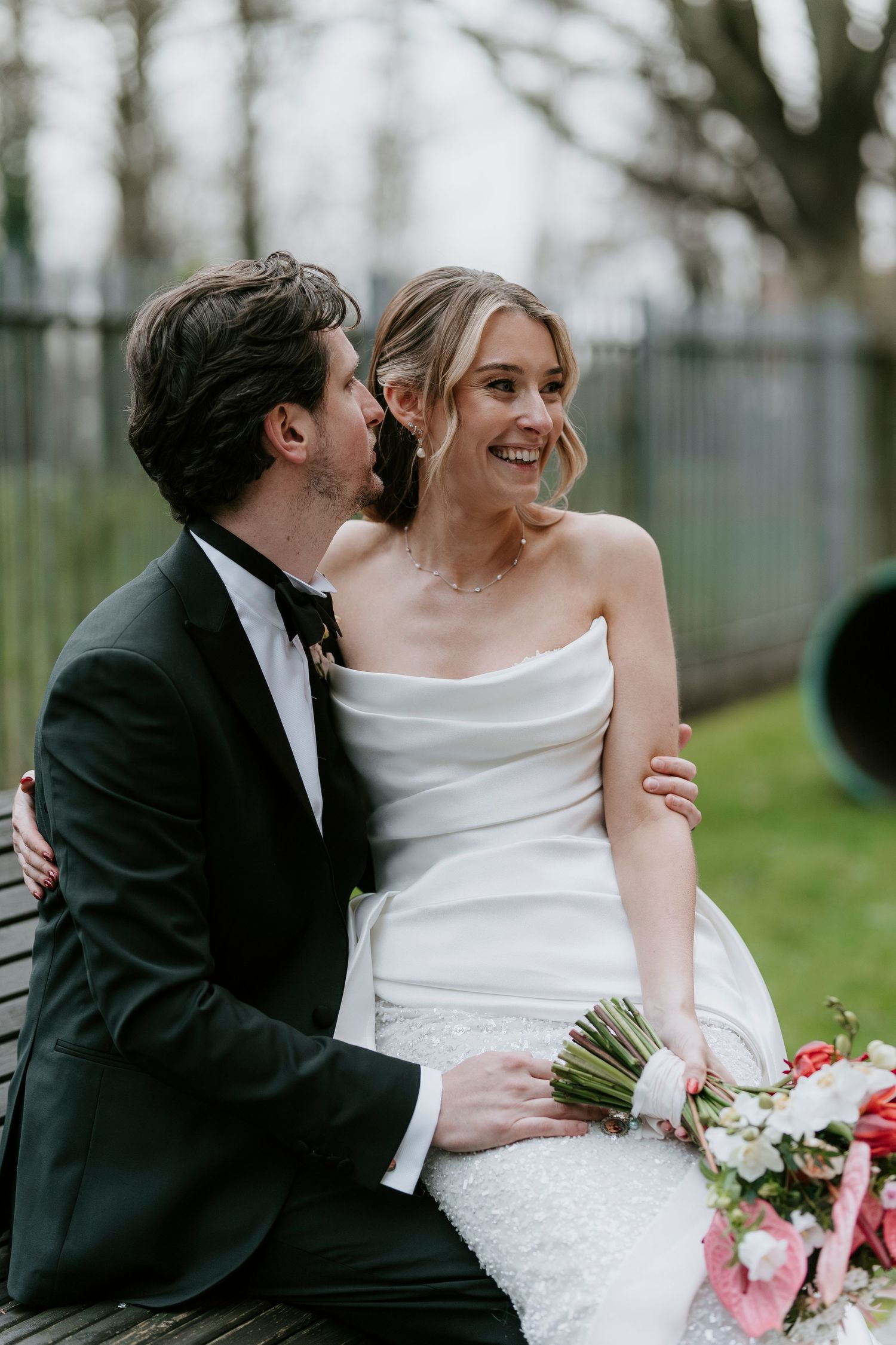 A romantic moment between newlyweds in formal attire sharing laughter in an outdoor garden setting.