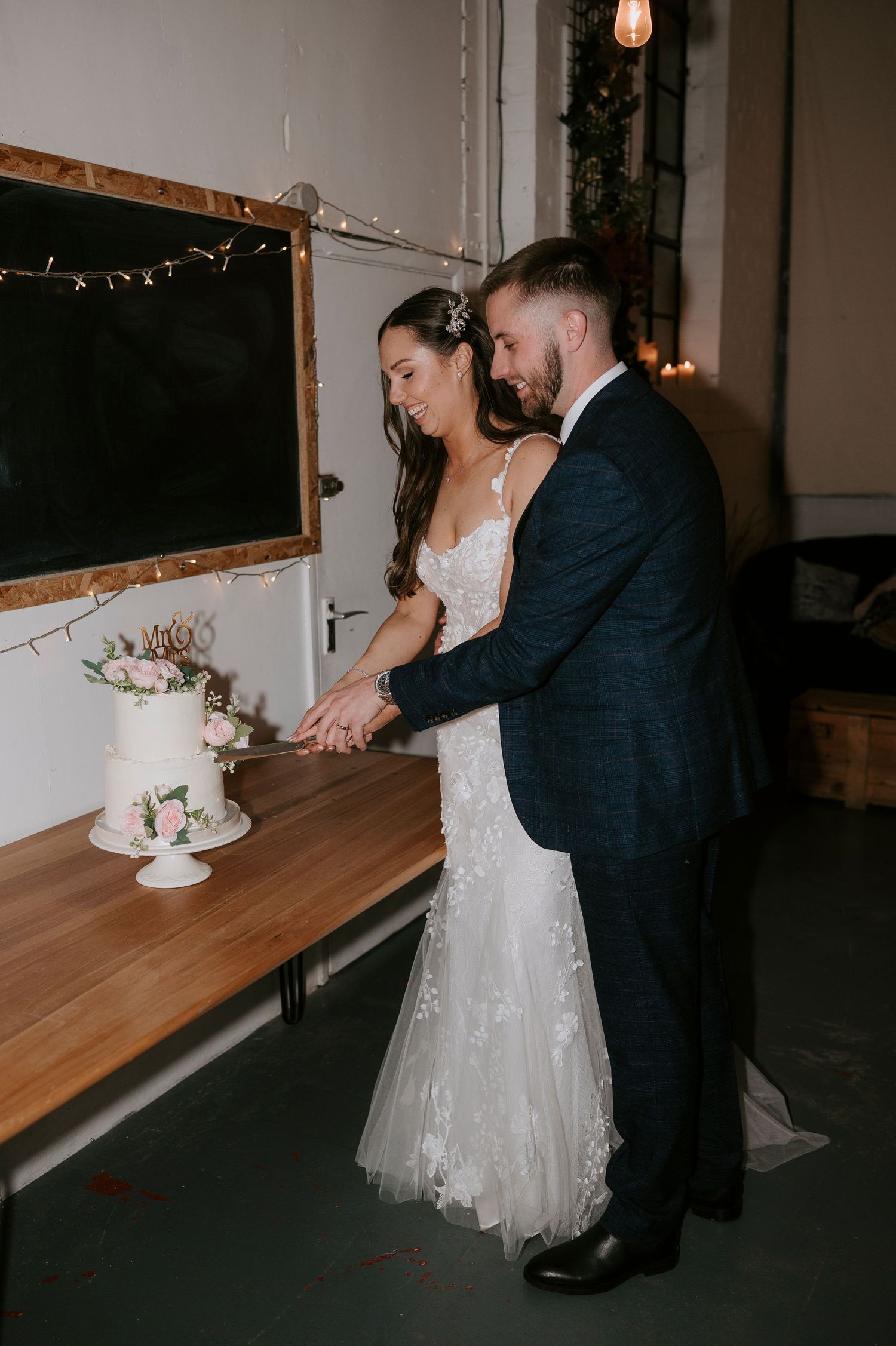 Bride and groom cutting their small white floral wedding cake together at their wedding reception.